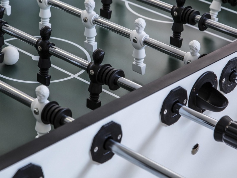 Close-up of a foosball table with black and white player figures on metal rods.