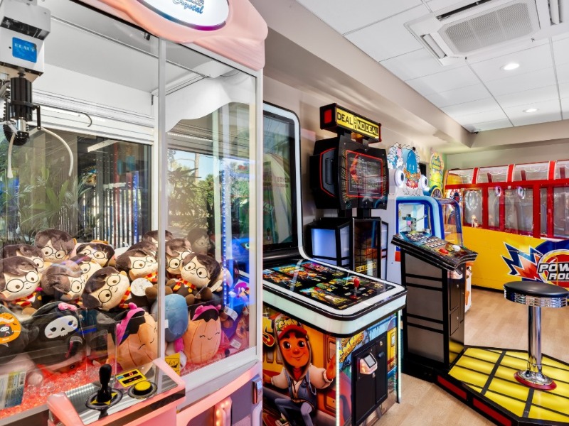 Arcade room with claw machine filled with plush toys and various game machines including Deal or No Deal.