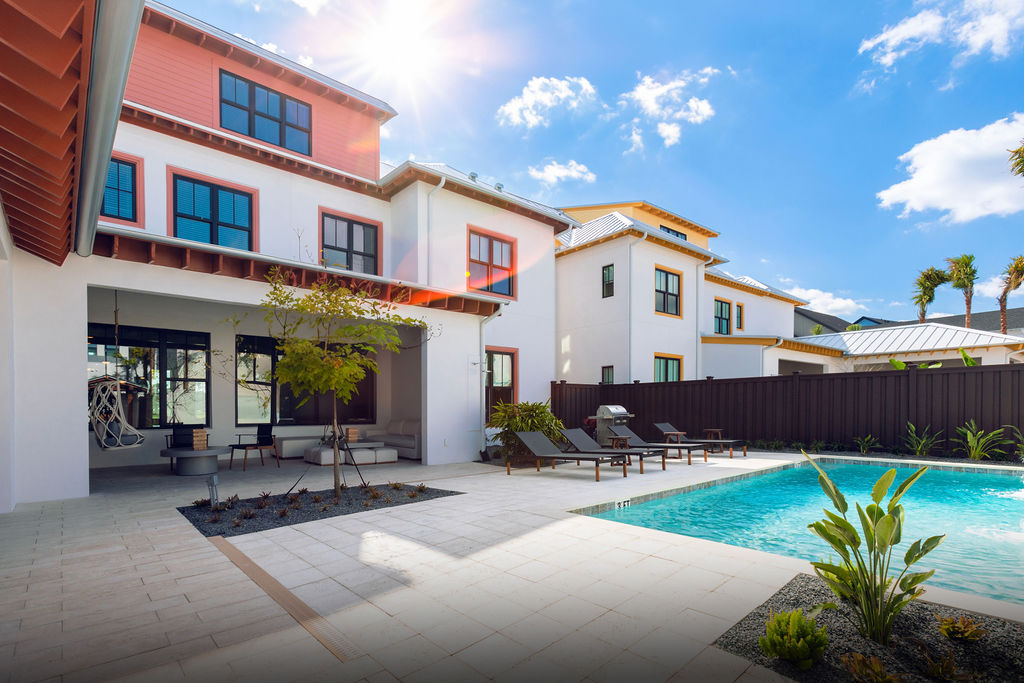 Modern white house patio with outdoor seating, sun loungers, and a swimming pool under blue sky.