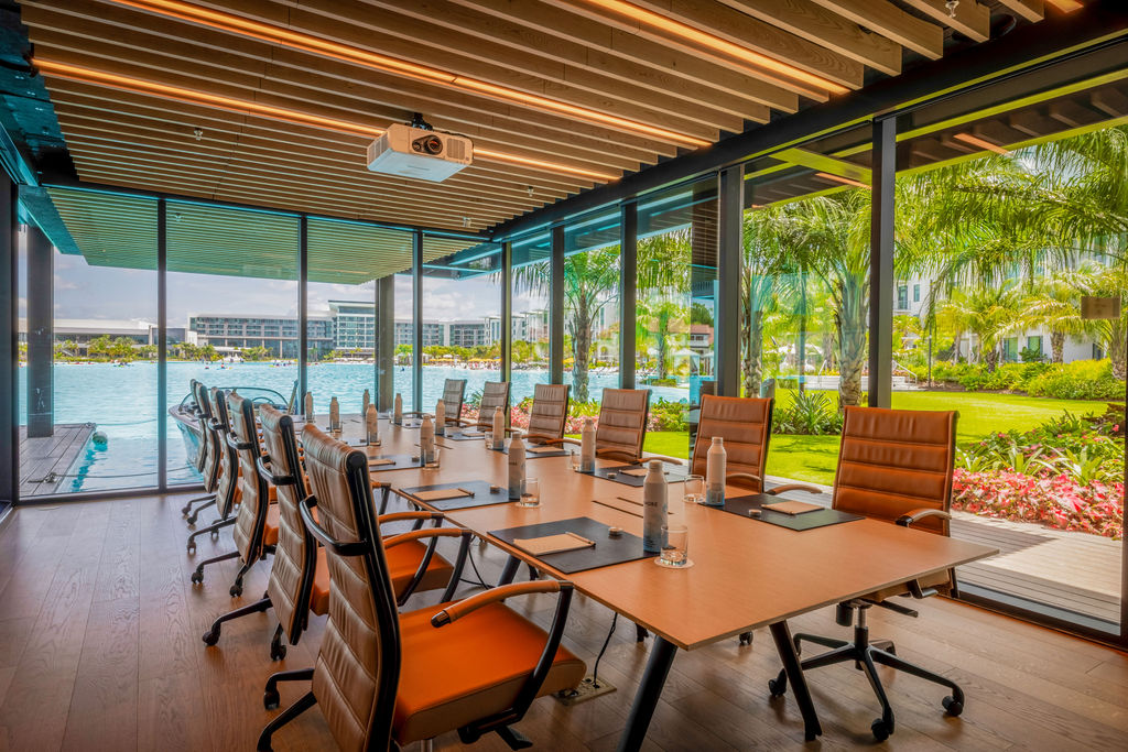 Modern conference room with glass walls overlooking a pool and lush greenery outside.