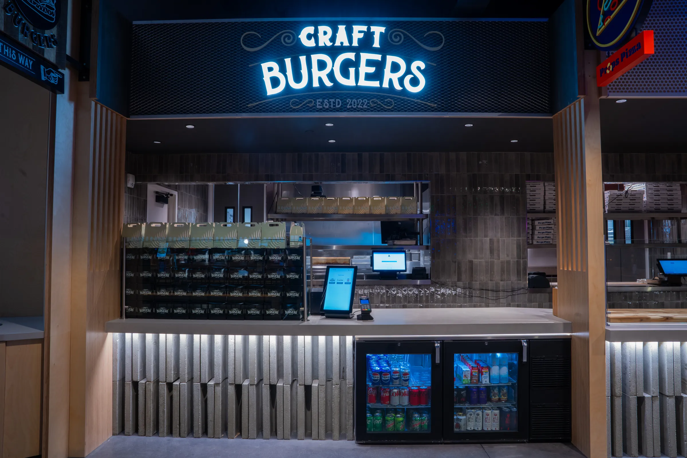Empty craft burger counter with branded packaging and refrigerated drinks underlit below the service area.