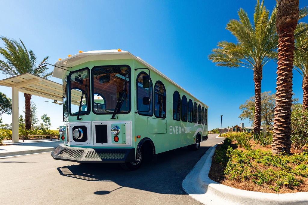 Green tour trolley labeled Evermore parked on a road with palm trees and shrubs nearby under clear sky.