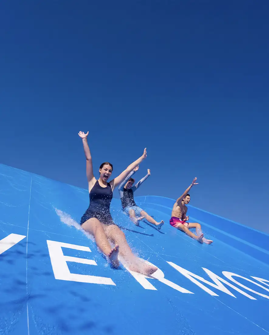 Three people sliding down a large blue water slide with arms raised, splashing water.