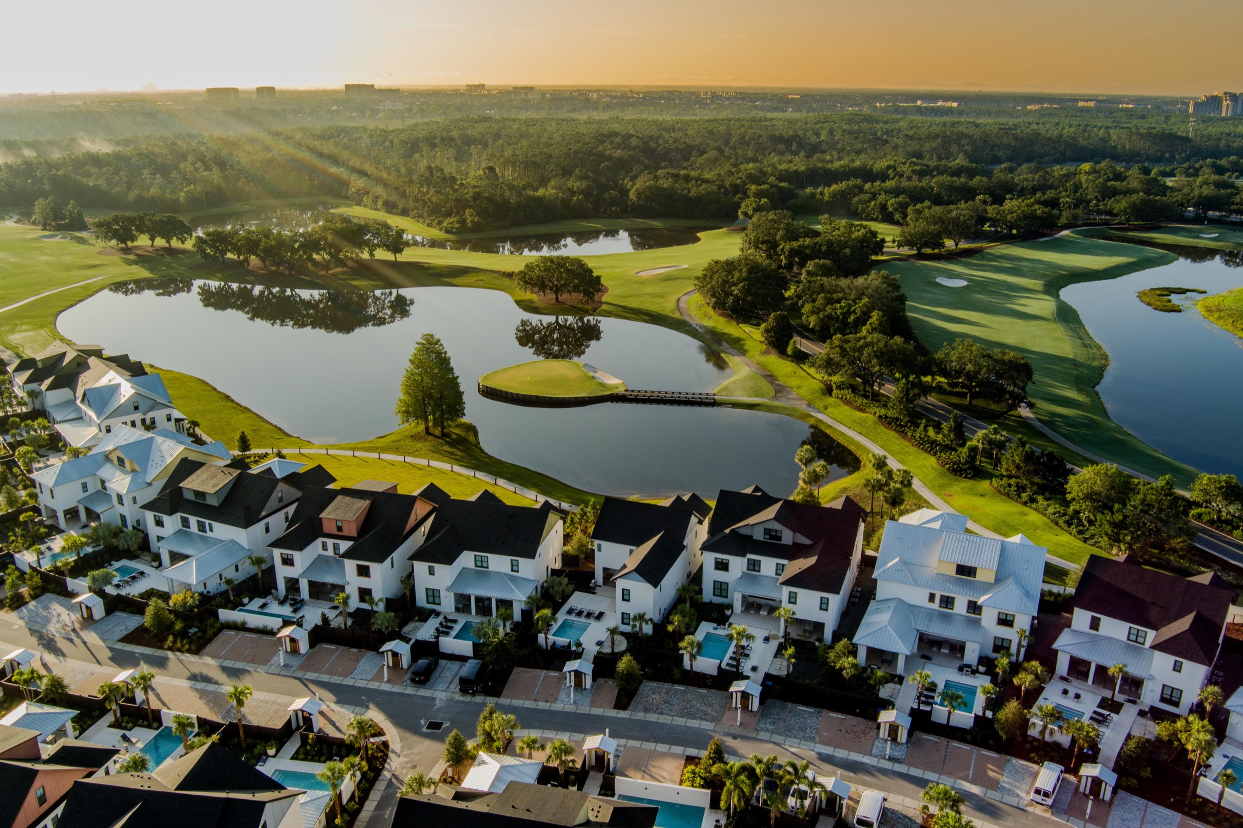 Aerial view of a residential neighborhood next to a golf course with water hazards and greenery at sunset.