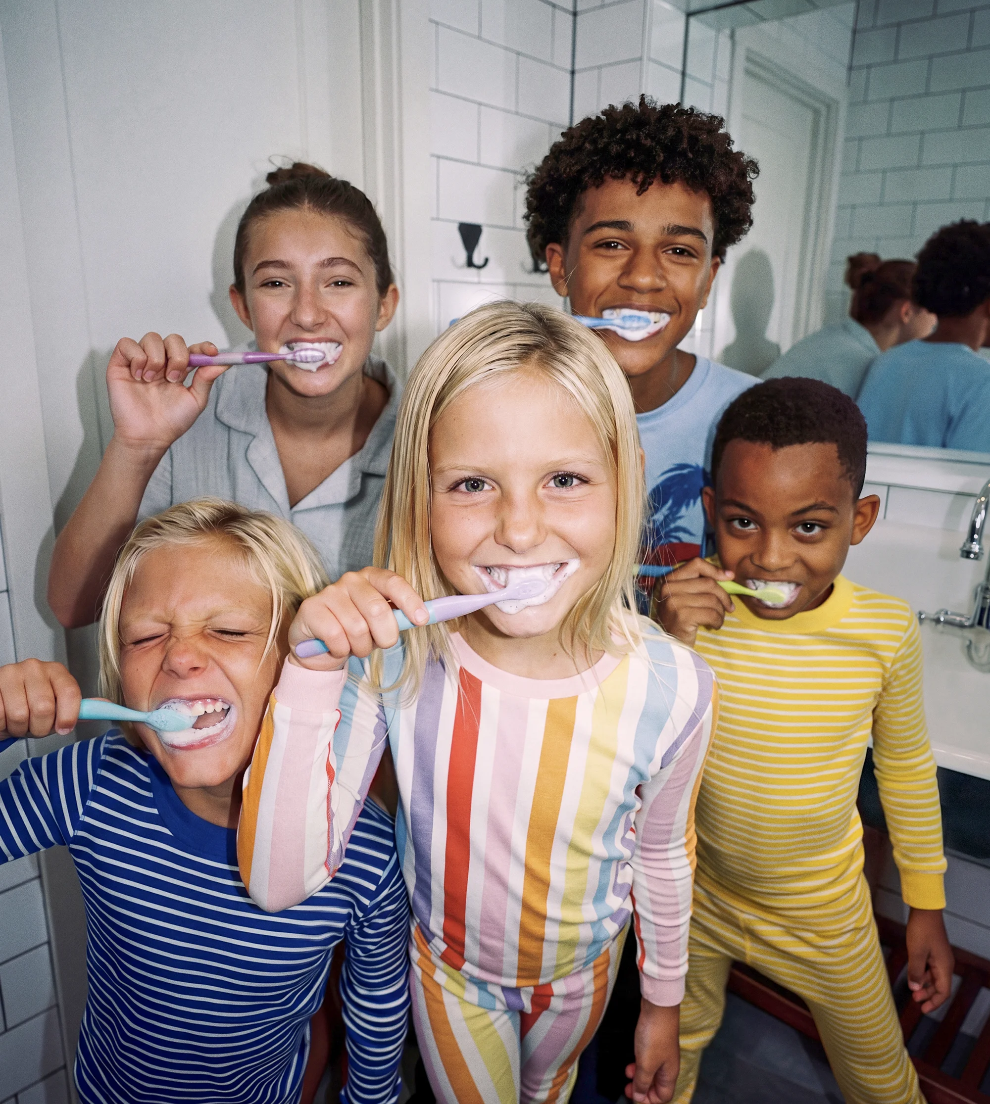 Five kids in colorful striped pajamas brushing their teeth in a bright bathroom together.