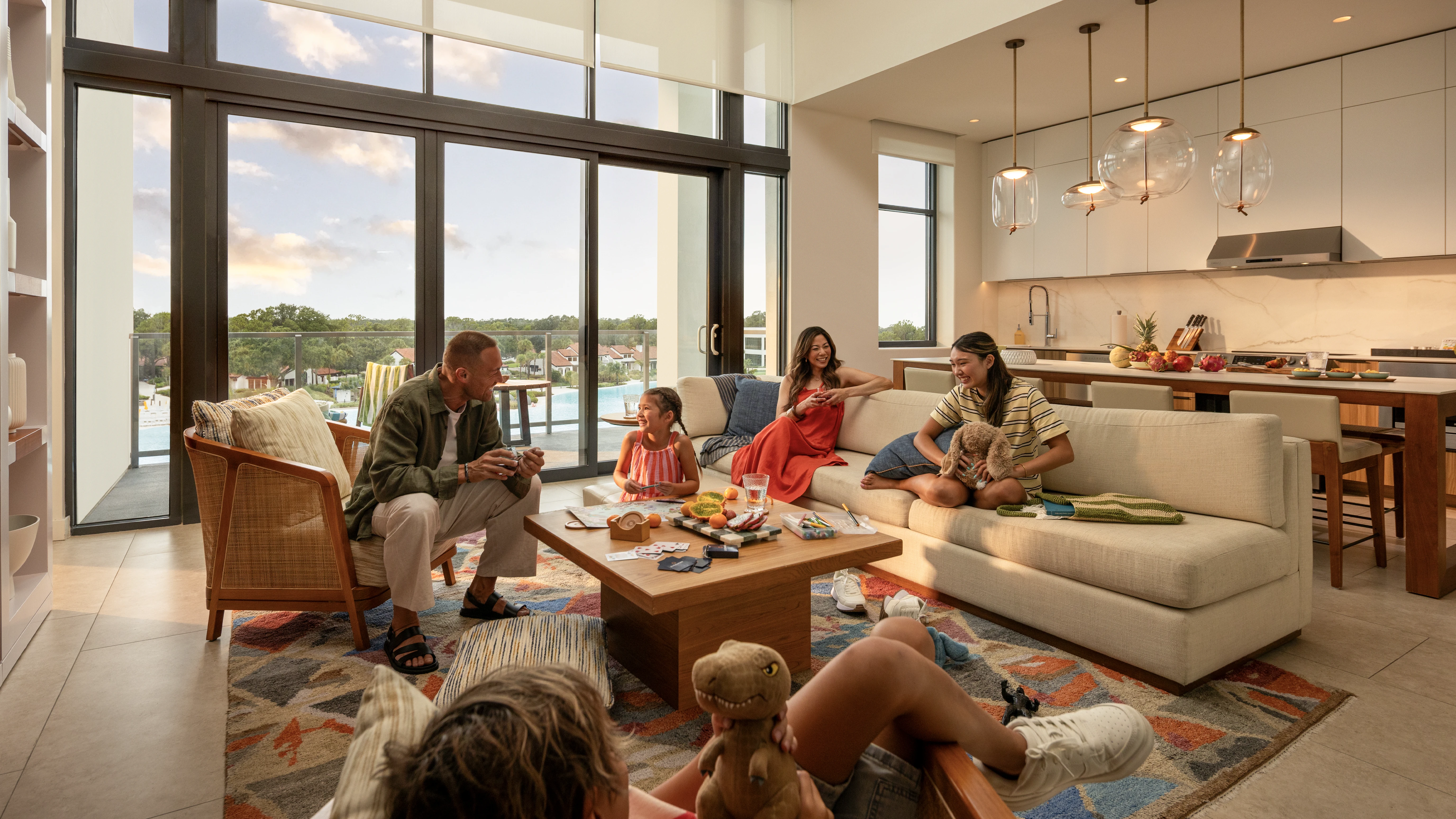 Family spending time together in a modern living room with large windows and an open kitchen.