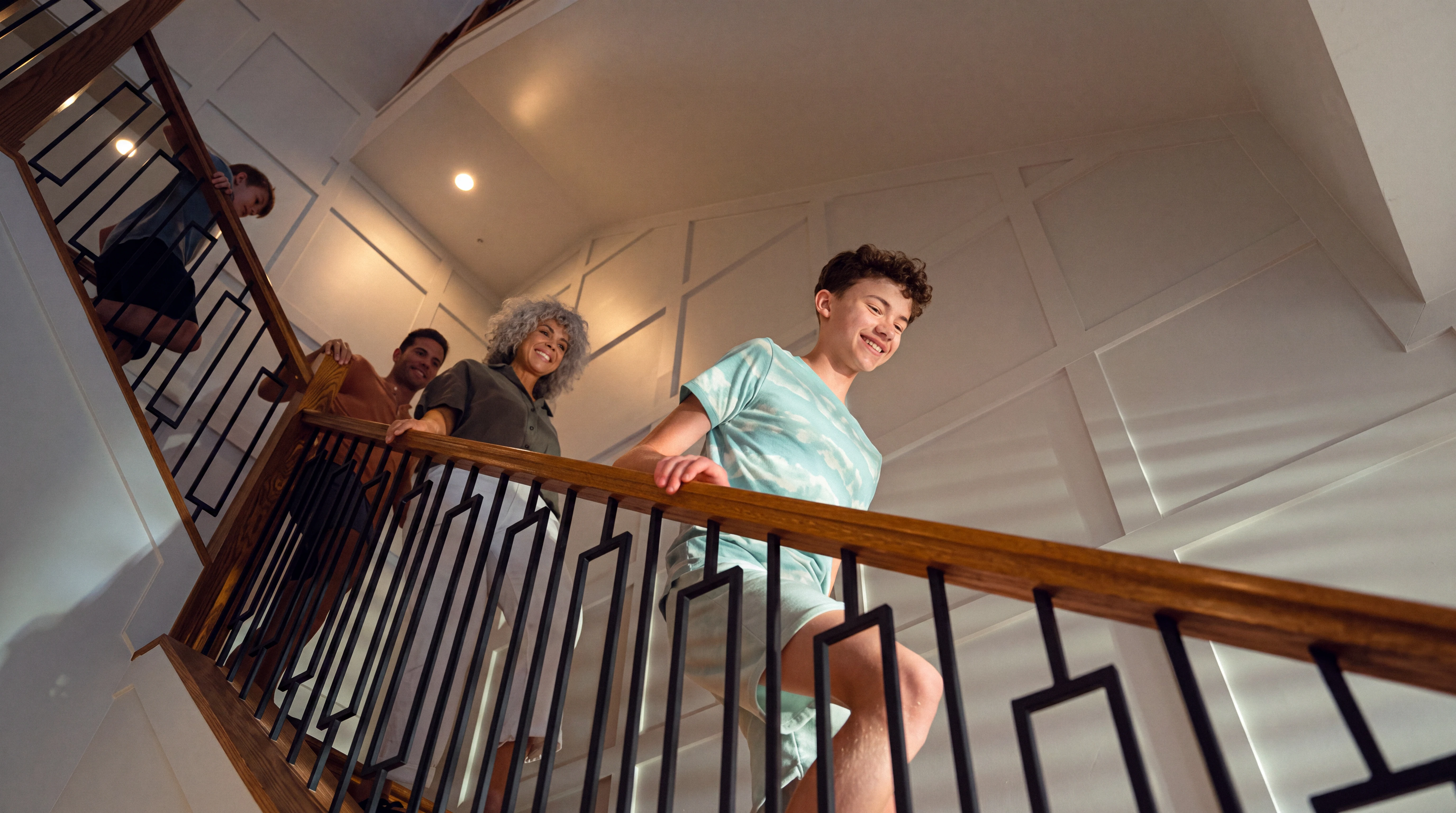 Smiling family walking down indoor stairs with a wooden handrail and decorative wall panels.