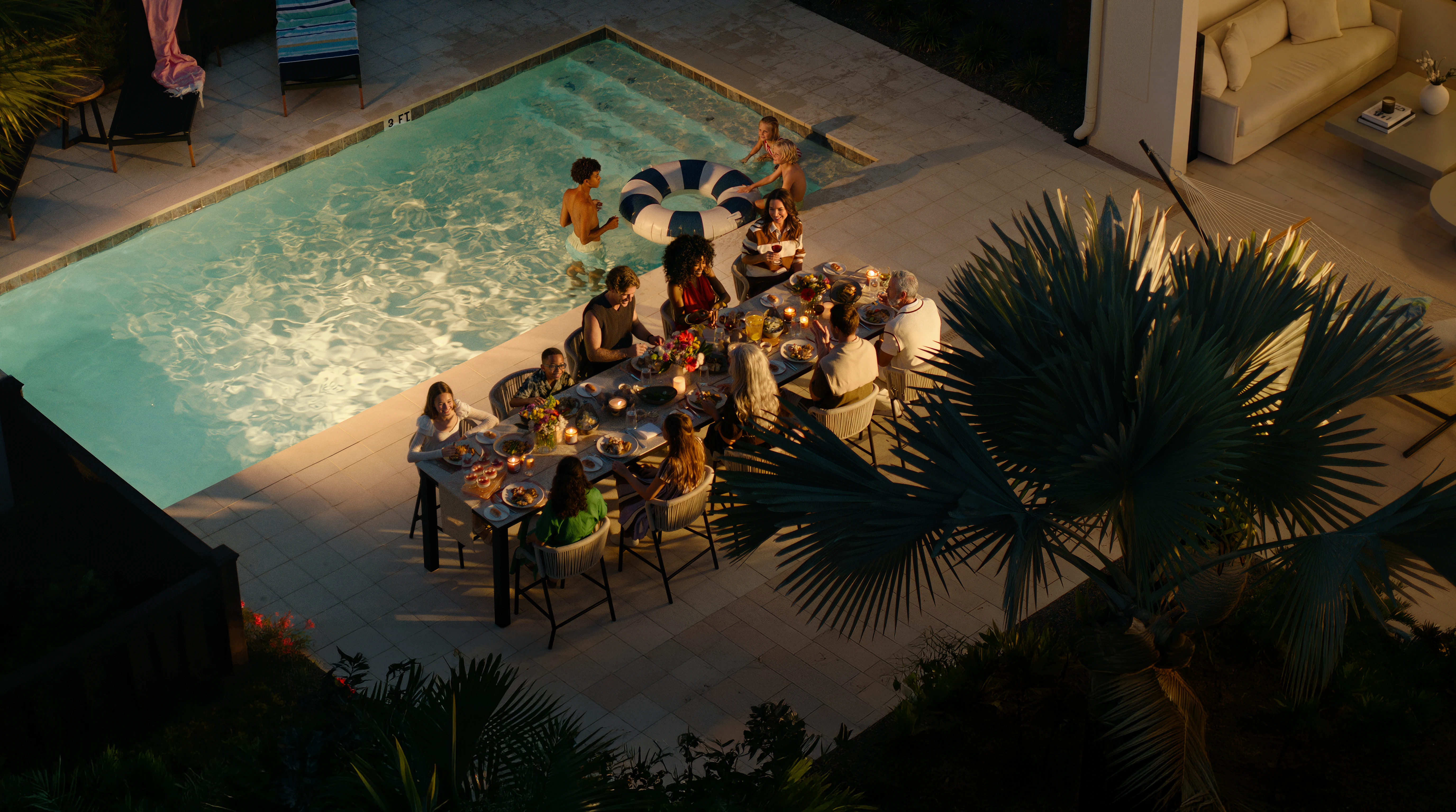 Family and friends enjoying a late evening outdoor dinner by a pool.