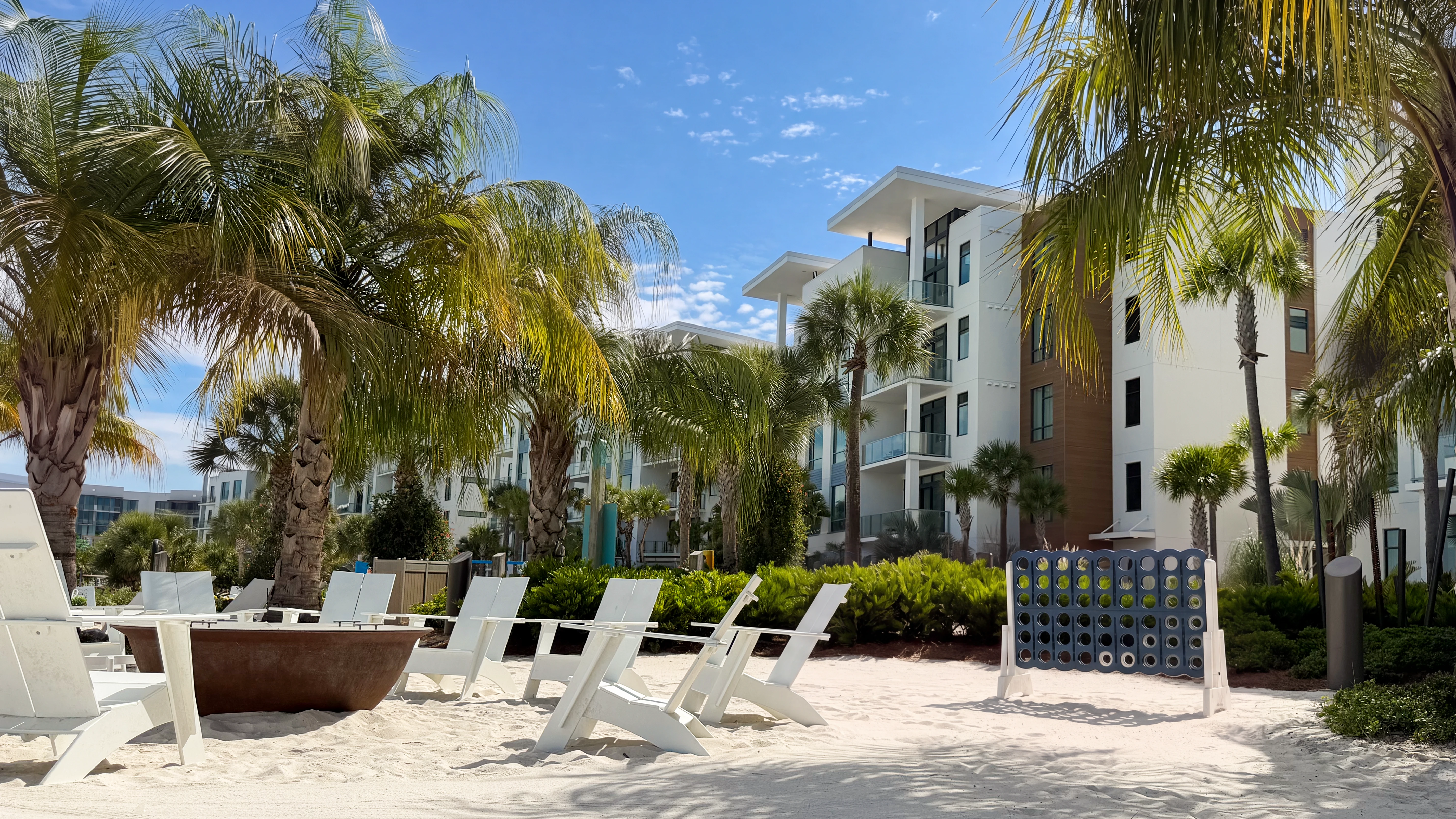 Outdoor seating with white chairs around fire pit and large connect four game by palm trees by Evermore Flats.