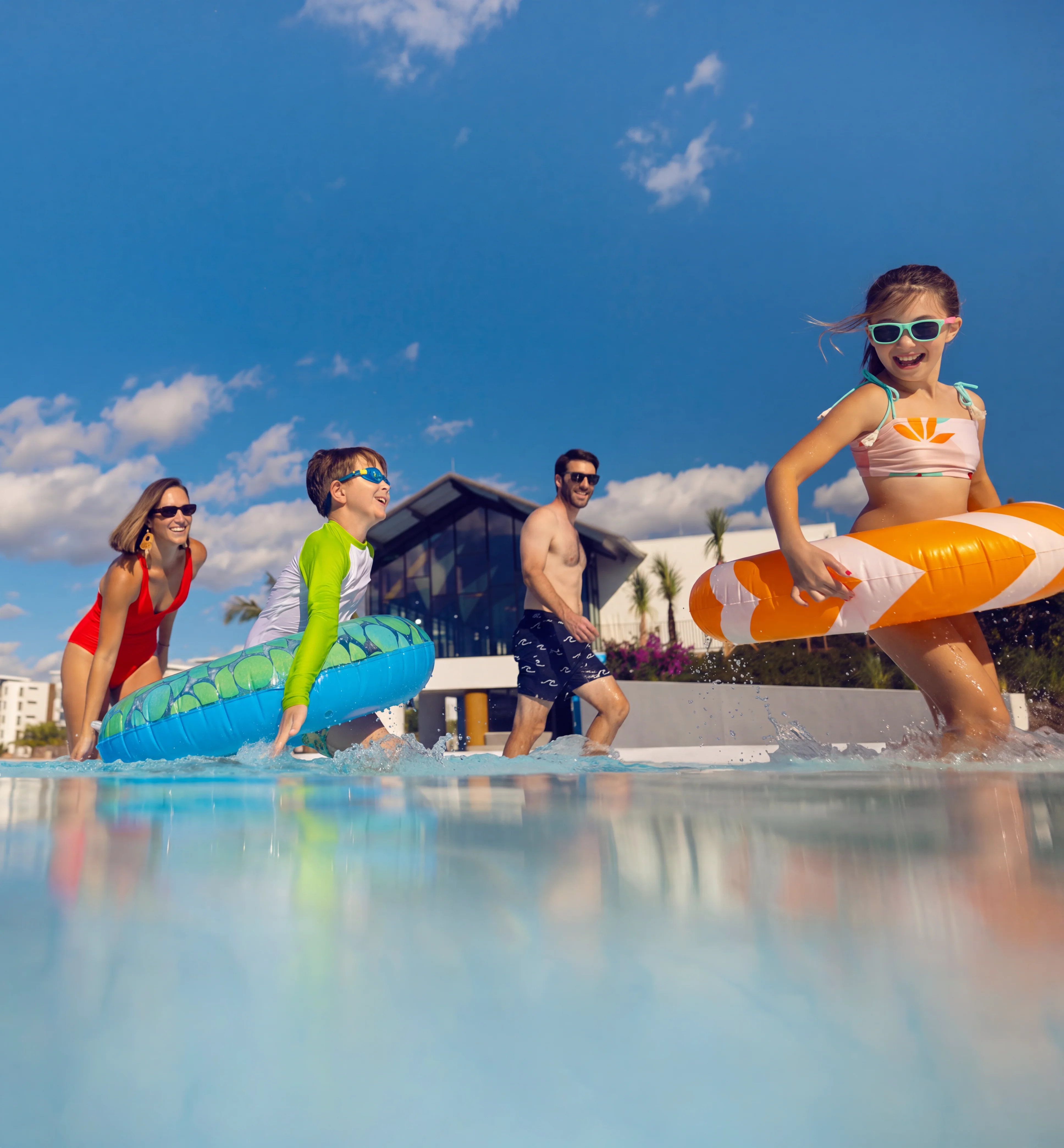 Family of four wearing sunglasses playing with floaties in the Evermore Bay under a sunny blue sky.