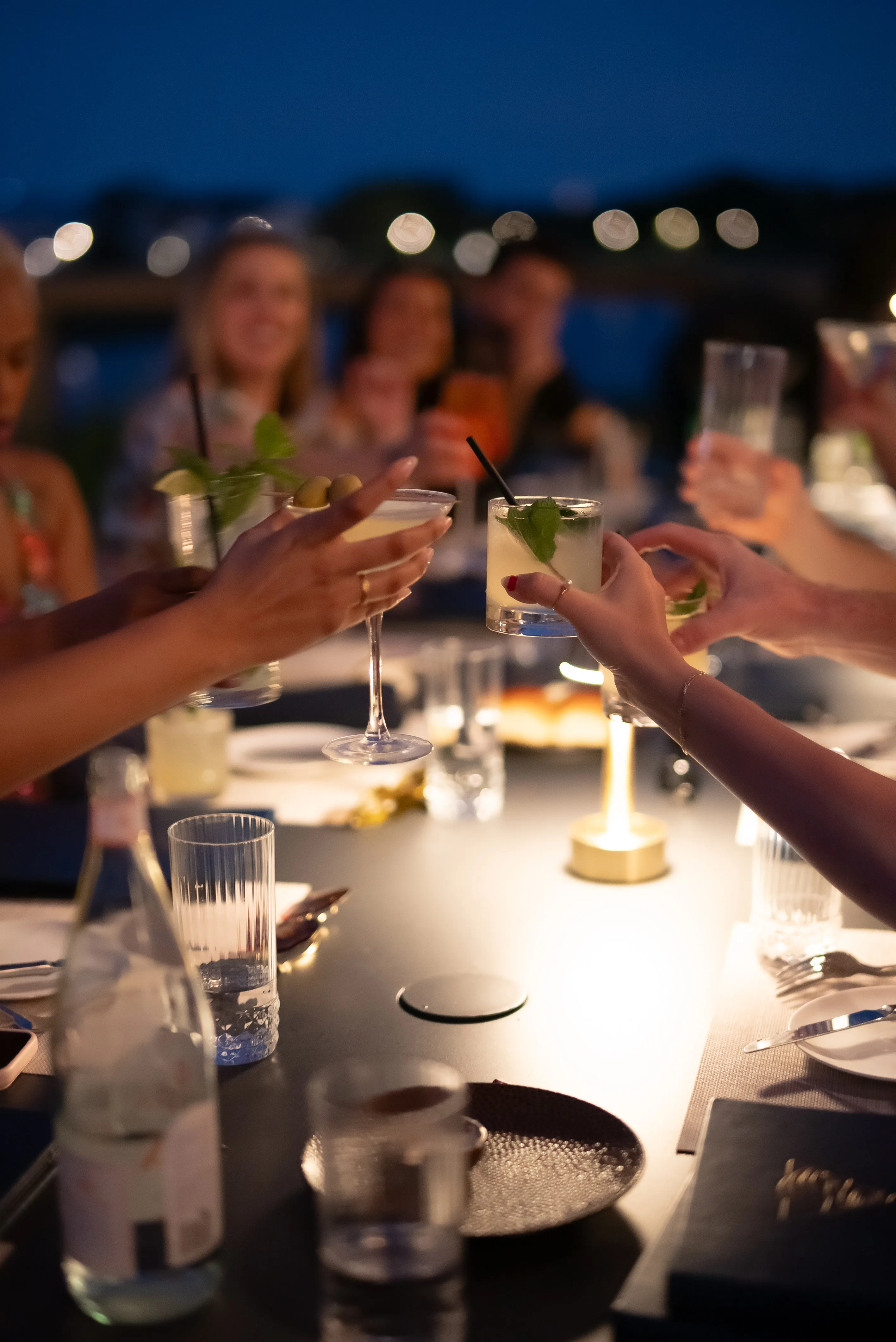 People clinking cocktail glasses in a dimly lit outdoor evening gathering.