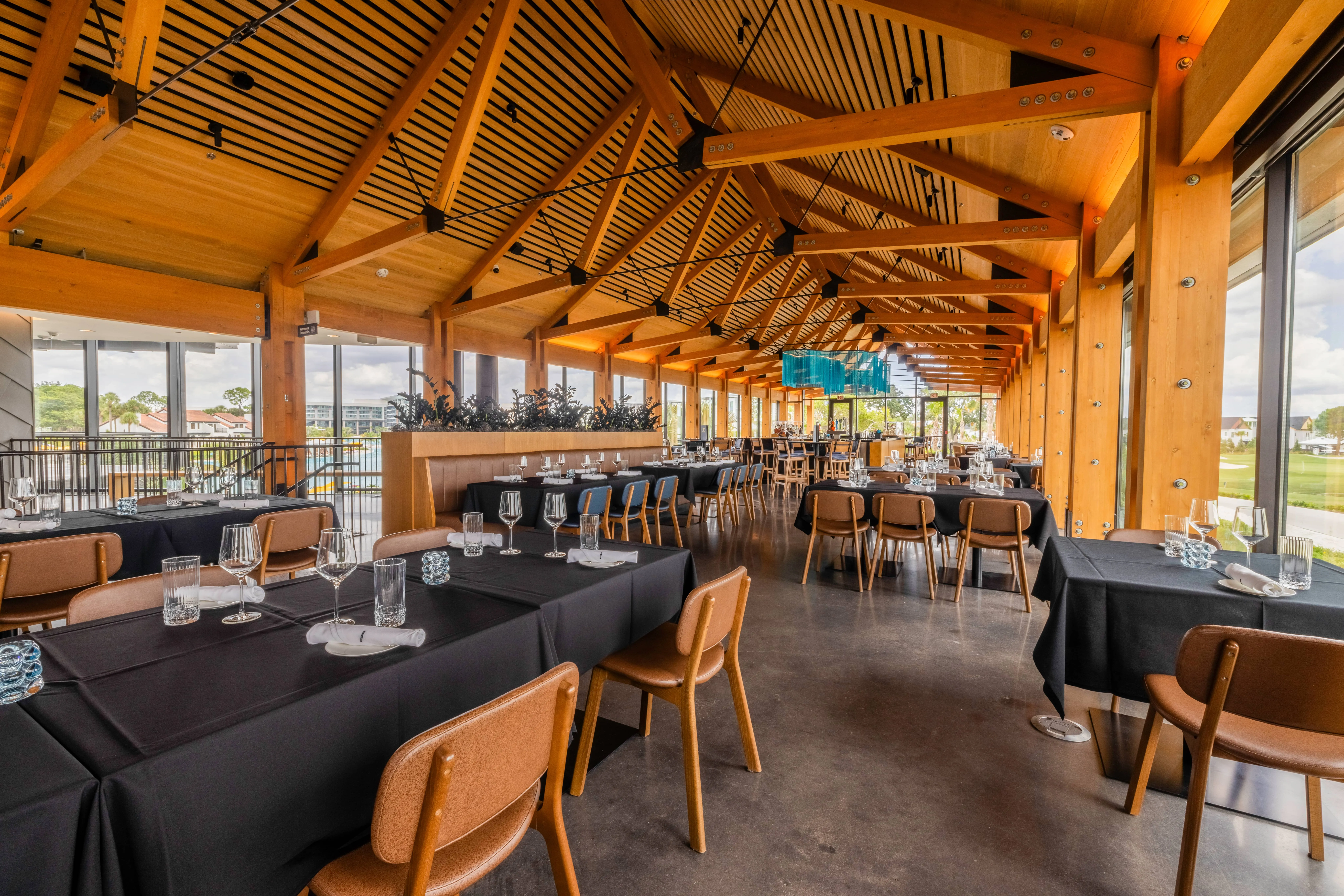 Spacious restaurant with wooden beams, black tablecloths, and large windows overlooking greenery.