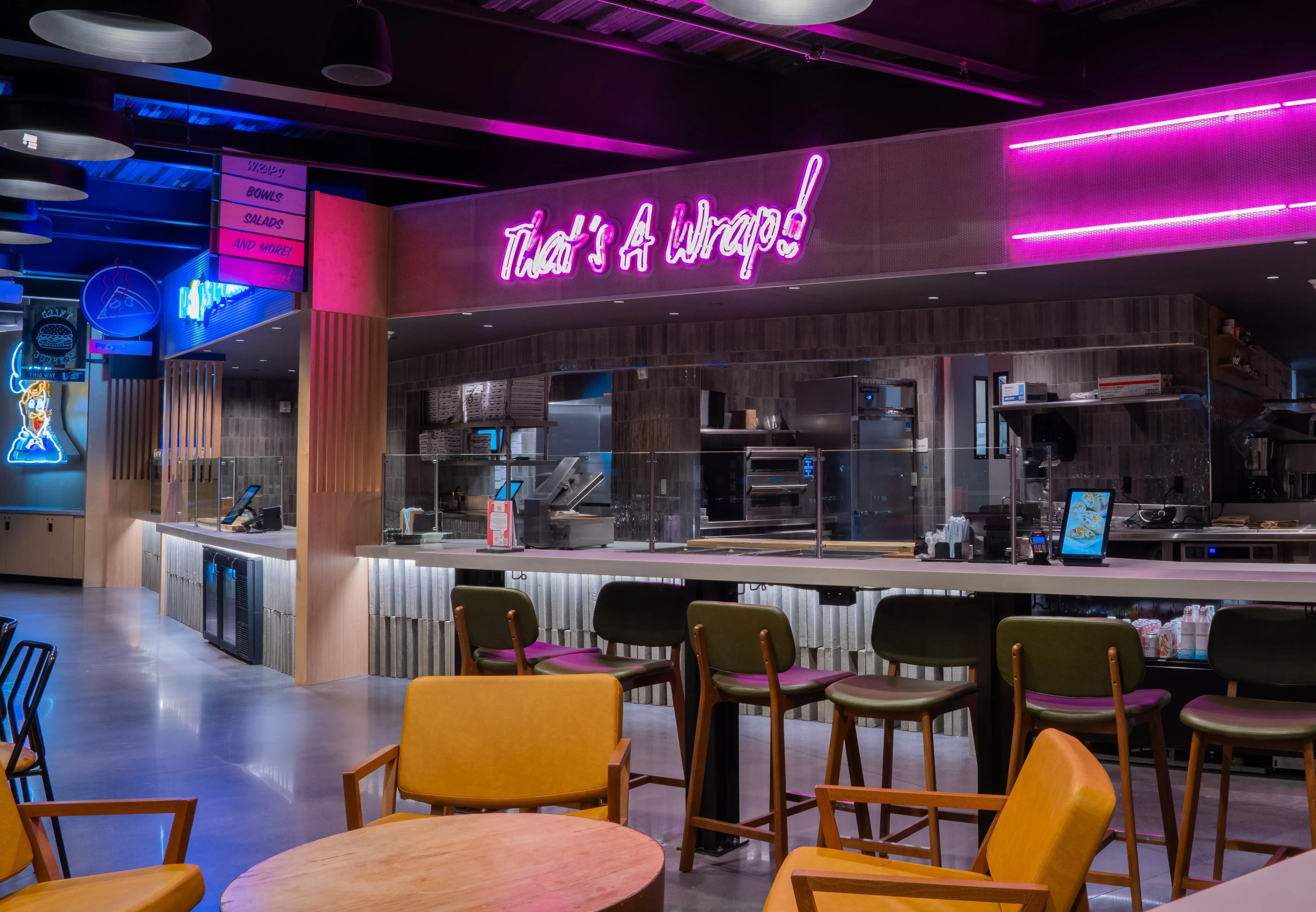 Modern restaurant counter with neon sign reading That's A Wrap!, seating area with chairs and tables.