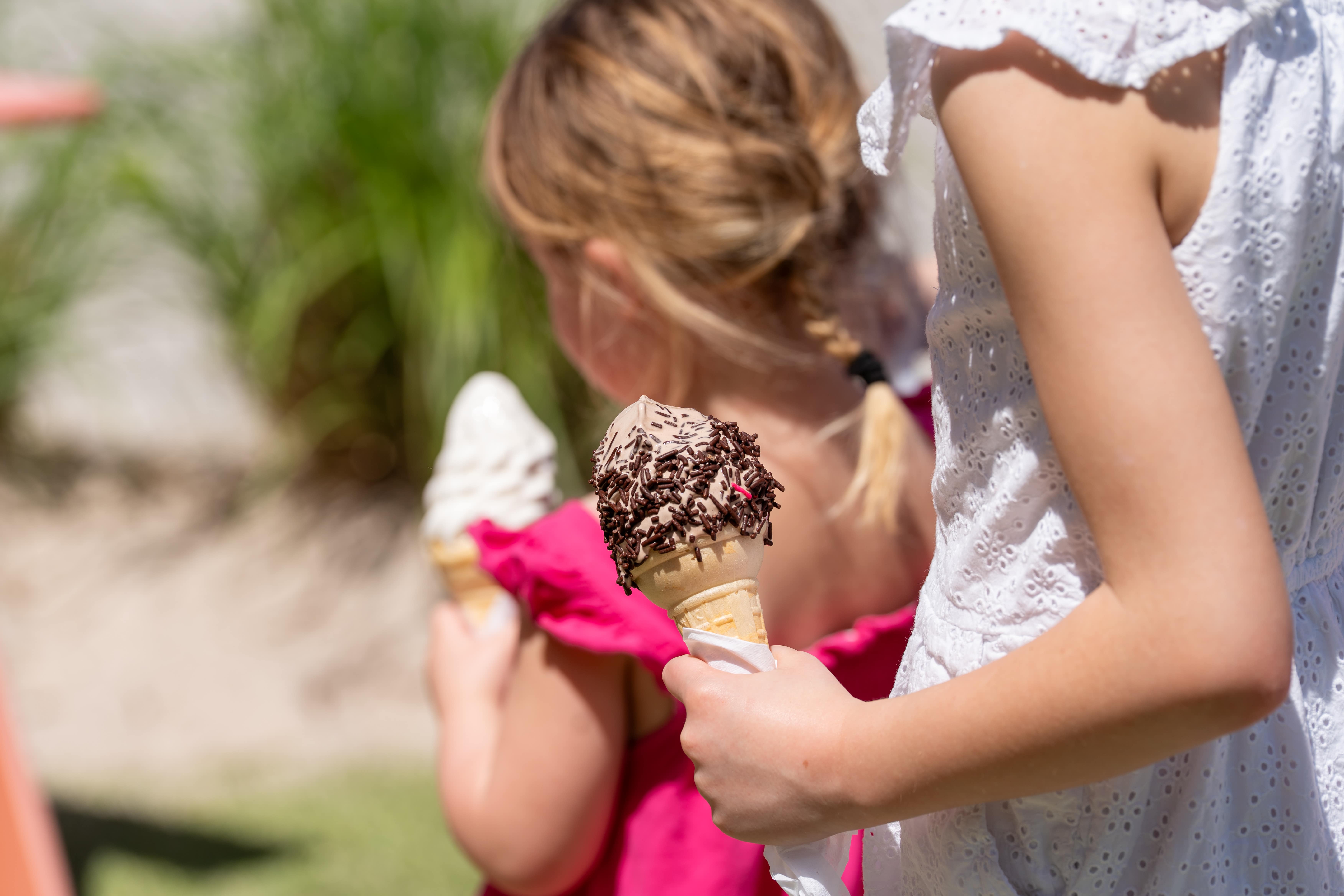 Two children holding ice cream cones, one with chocolate sprinkles, outdoors on a sunny day.