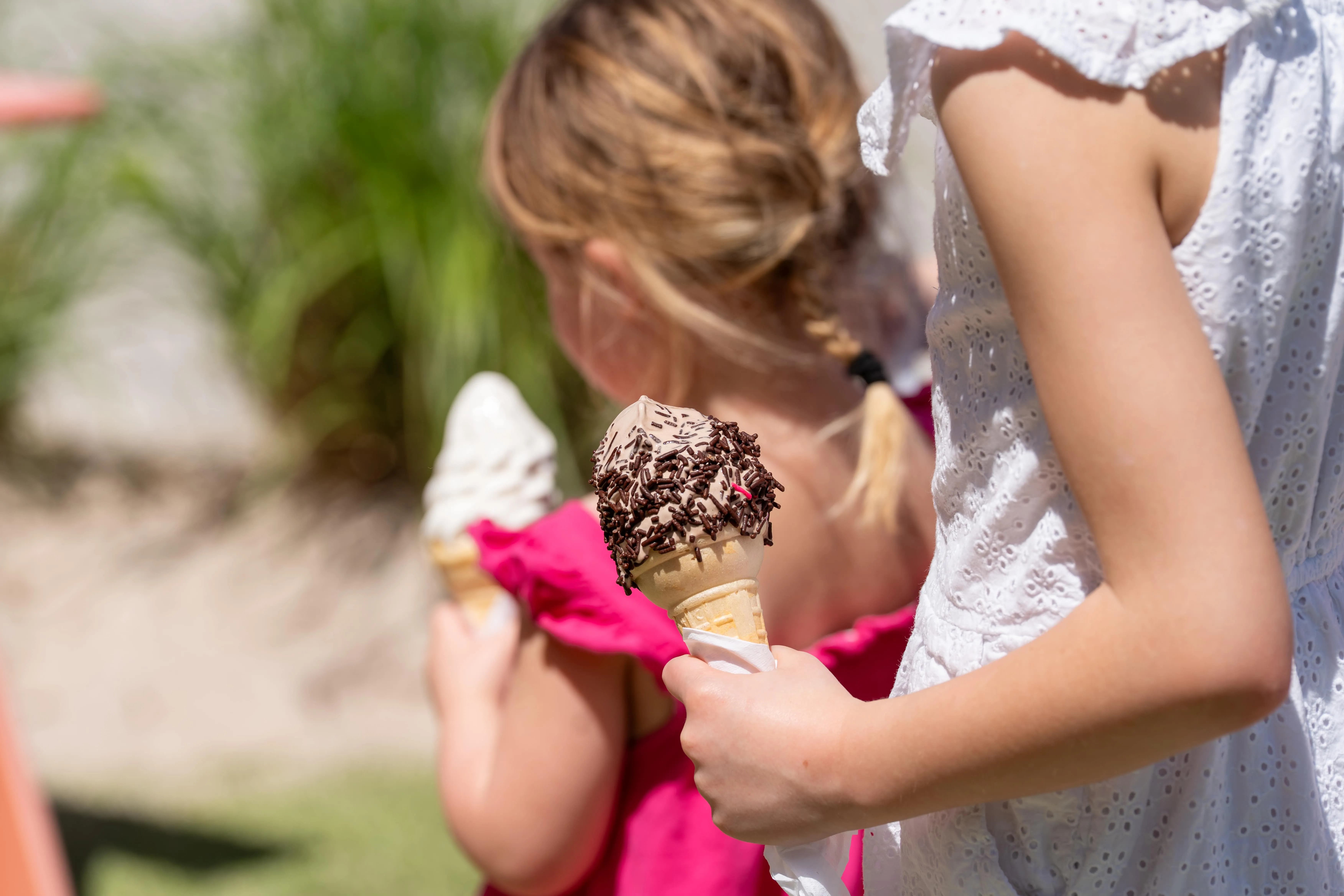 Two children holding ice cream cones, one with chocolate sprinkles, outdoors on a sunny day.