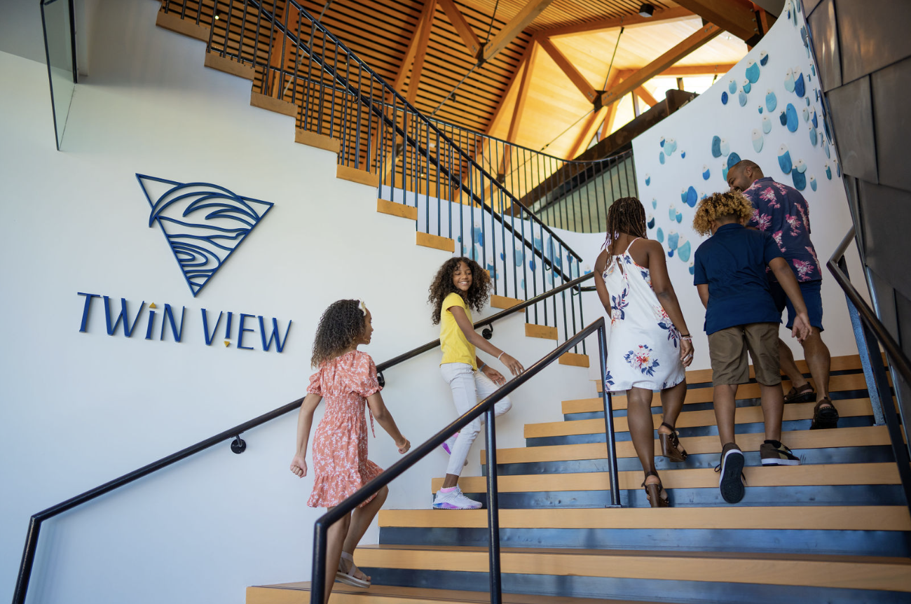 Family of five walking up wooden stairs inside building with Twin View logo on the wall.