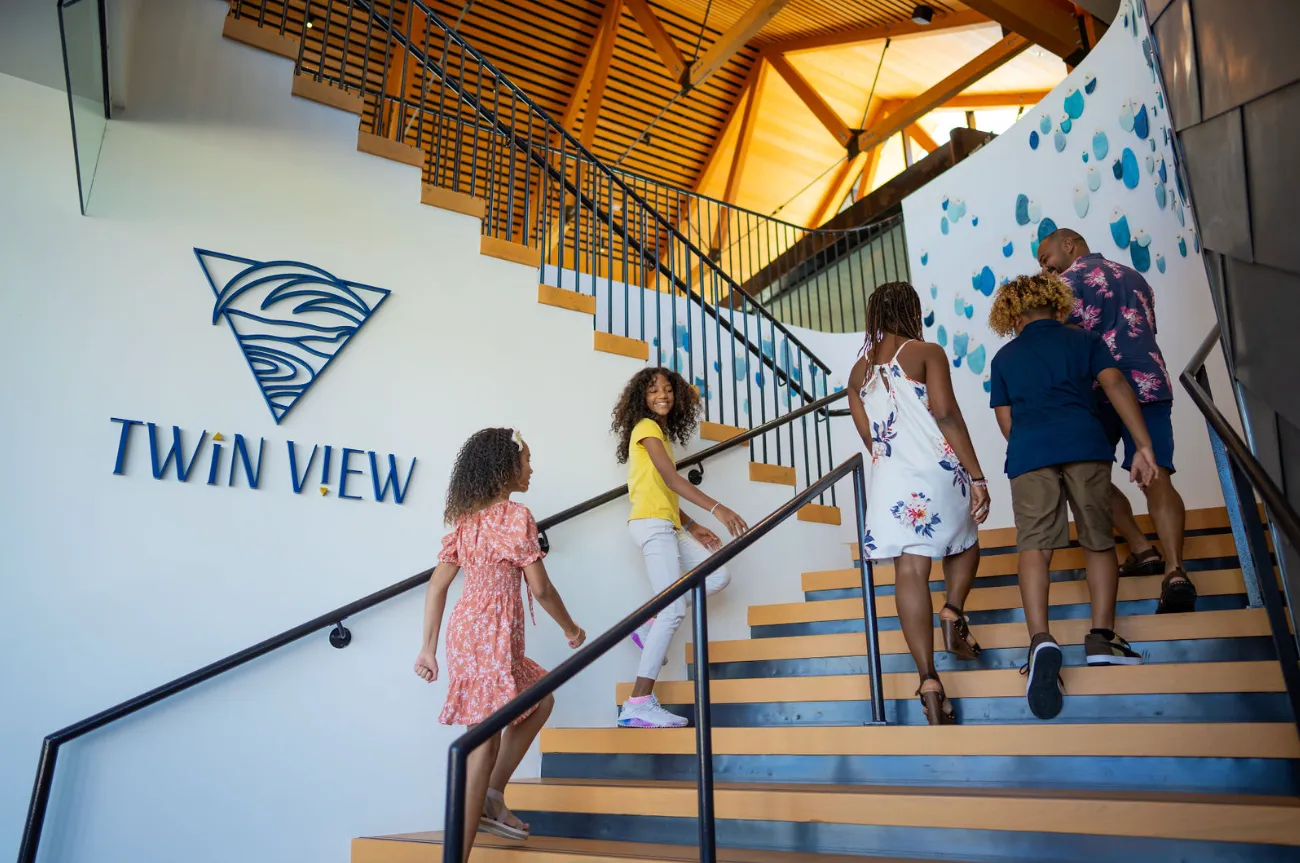 Family of five walking up wooden stairs inside building with Twin View logo on the wall.