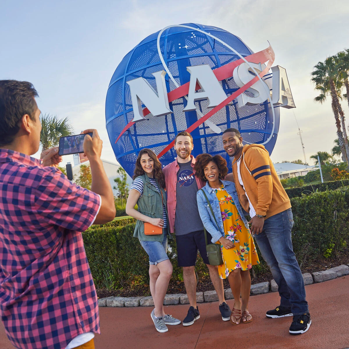 Four friends smiling and posing for a photo in front of a large NASA globe sign outdoors.