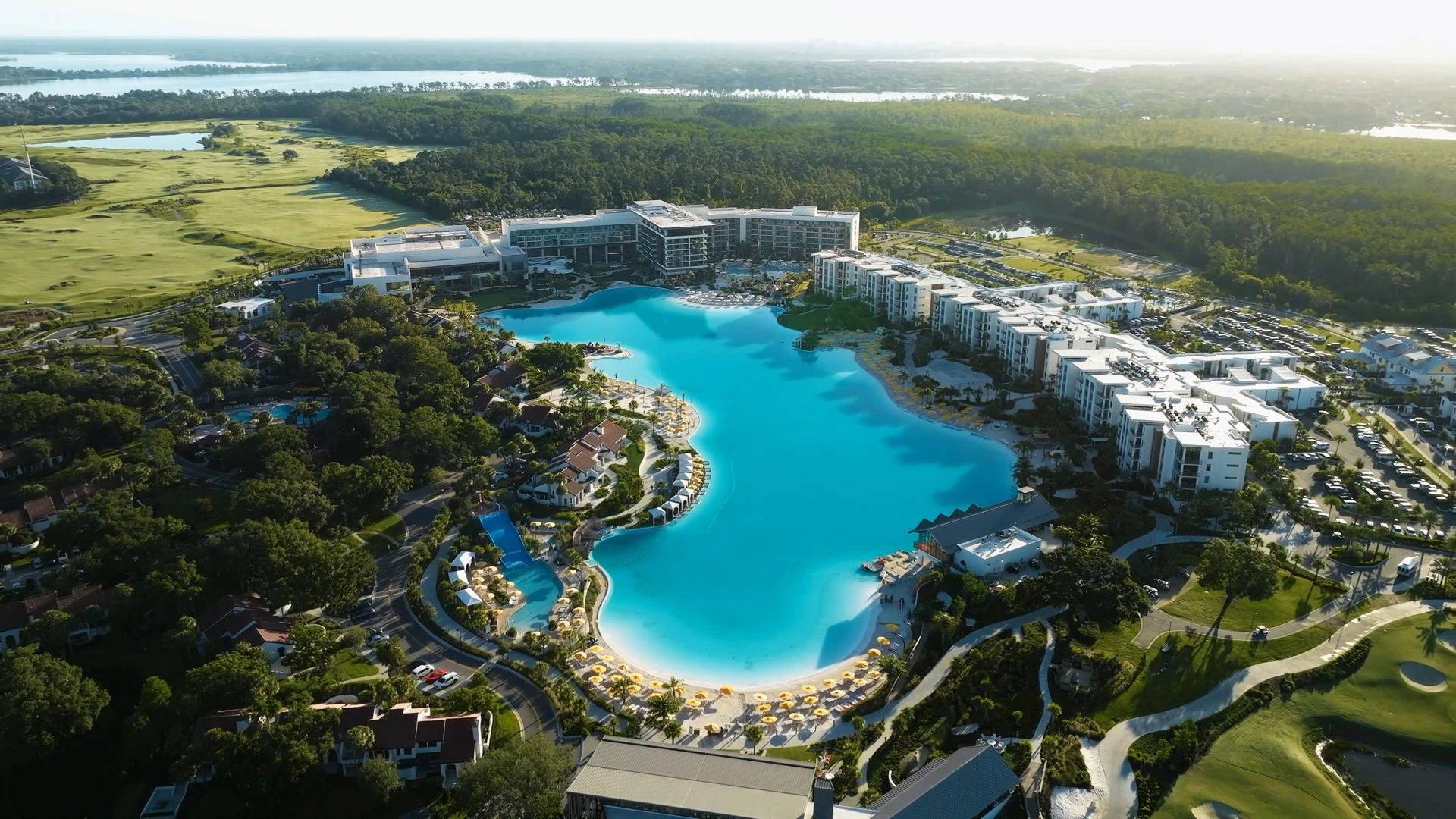 A large resort complex with a massive turquoise swimming pool surrounded by buildings, trees, and golf courses.