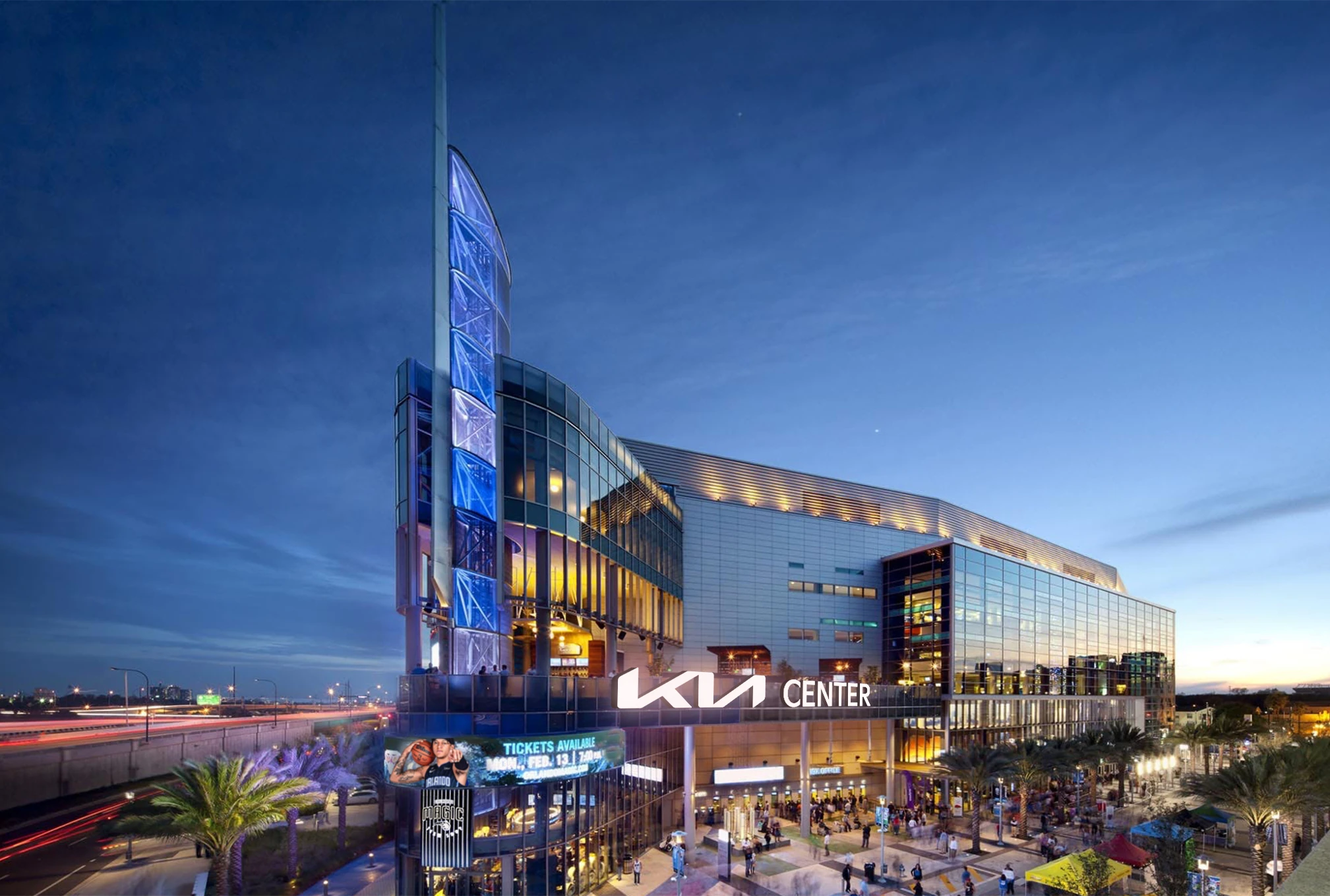 Evening view of Kia Center building with illuminated sign and people outside near palm trees.