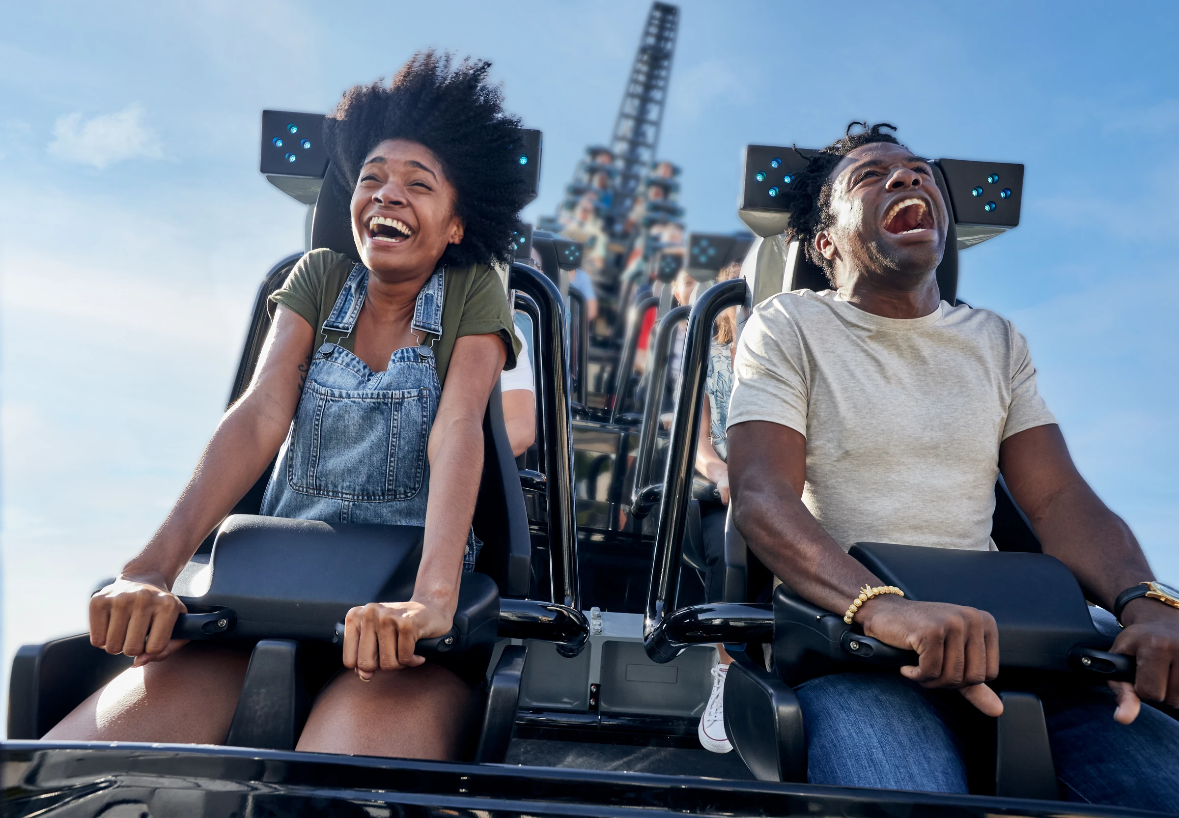 Two people laughing and gripping safety bars on a roller coaster ride under blue sky.