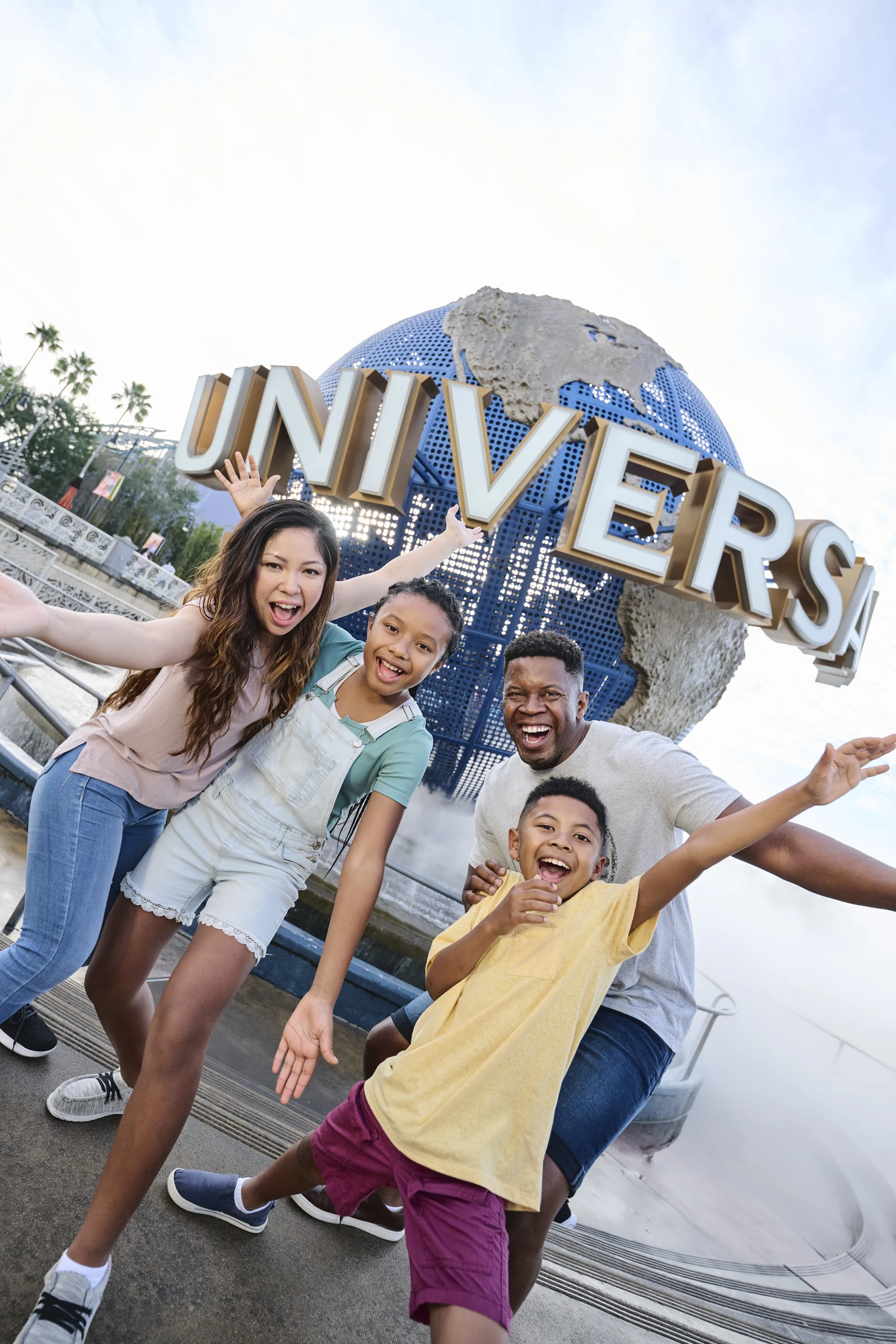 Happy diverse family posing excitedly in front of the Universal globe at a theme park.