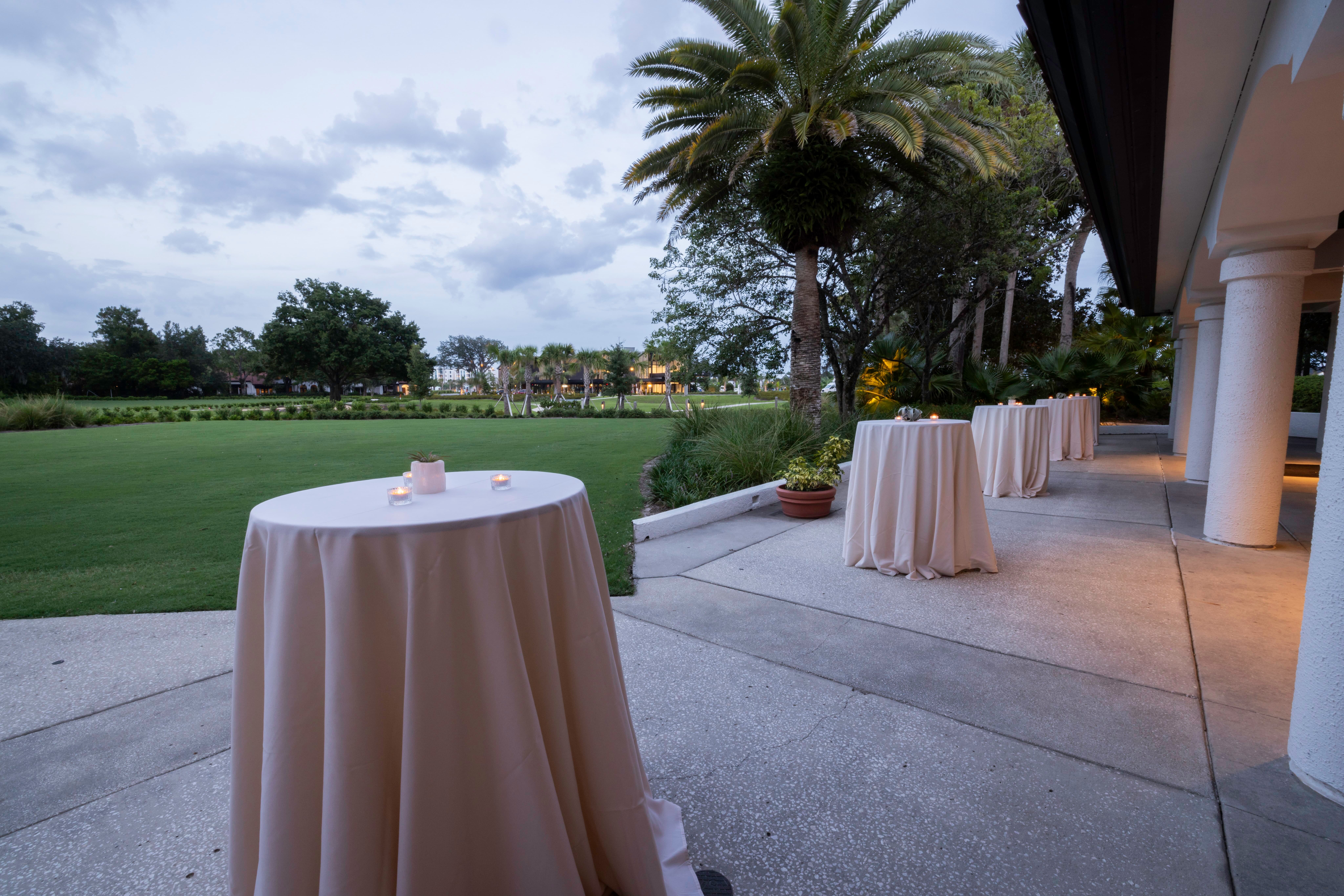 Outdoor patio with cocktail tables covered in beige cloth and small lit candles during dusk.
