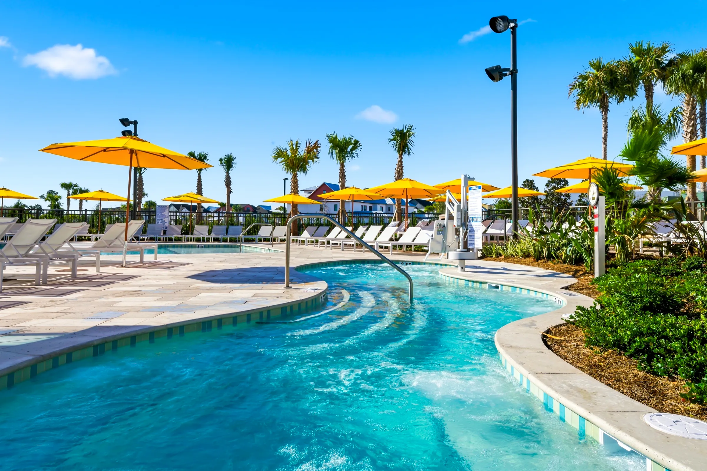 Outdoor pool with clear water, surrounded by white lounge chairs, yellow umbrellas, and palm trees.