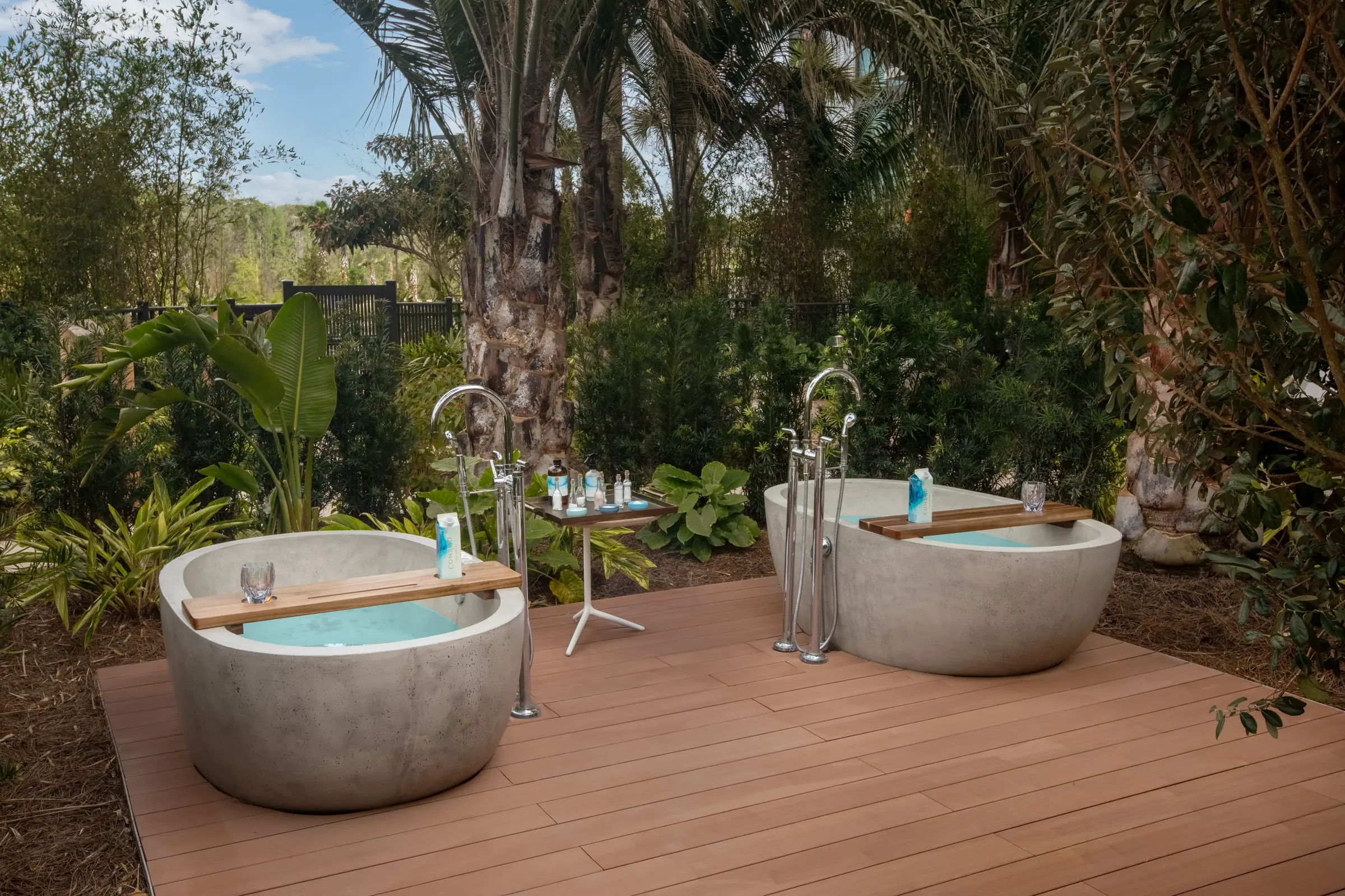 Two modern round outdoor soaking tubs on wooden deck surrounded by tropical greenery and palm trees.