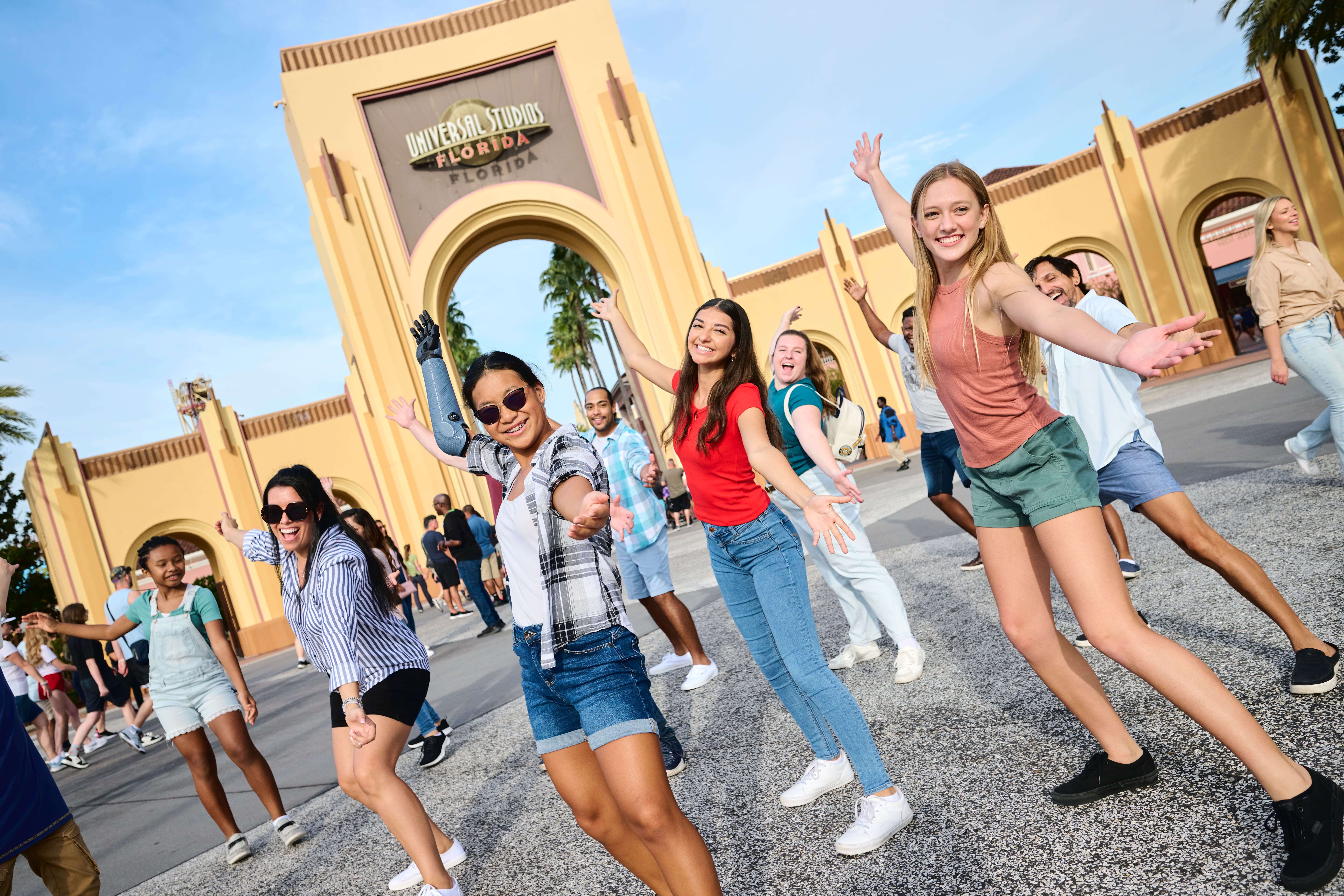 Group of diverse young people joyfully posing with arms outstretched at Universal Studios Florida entrance.