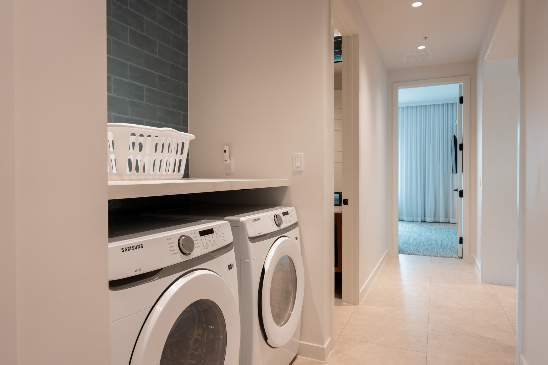Laundry area with Samsung washer and dryer under a counter and a white laundry basket on top.