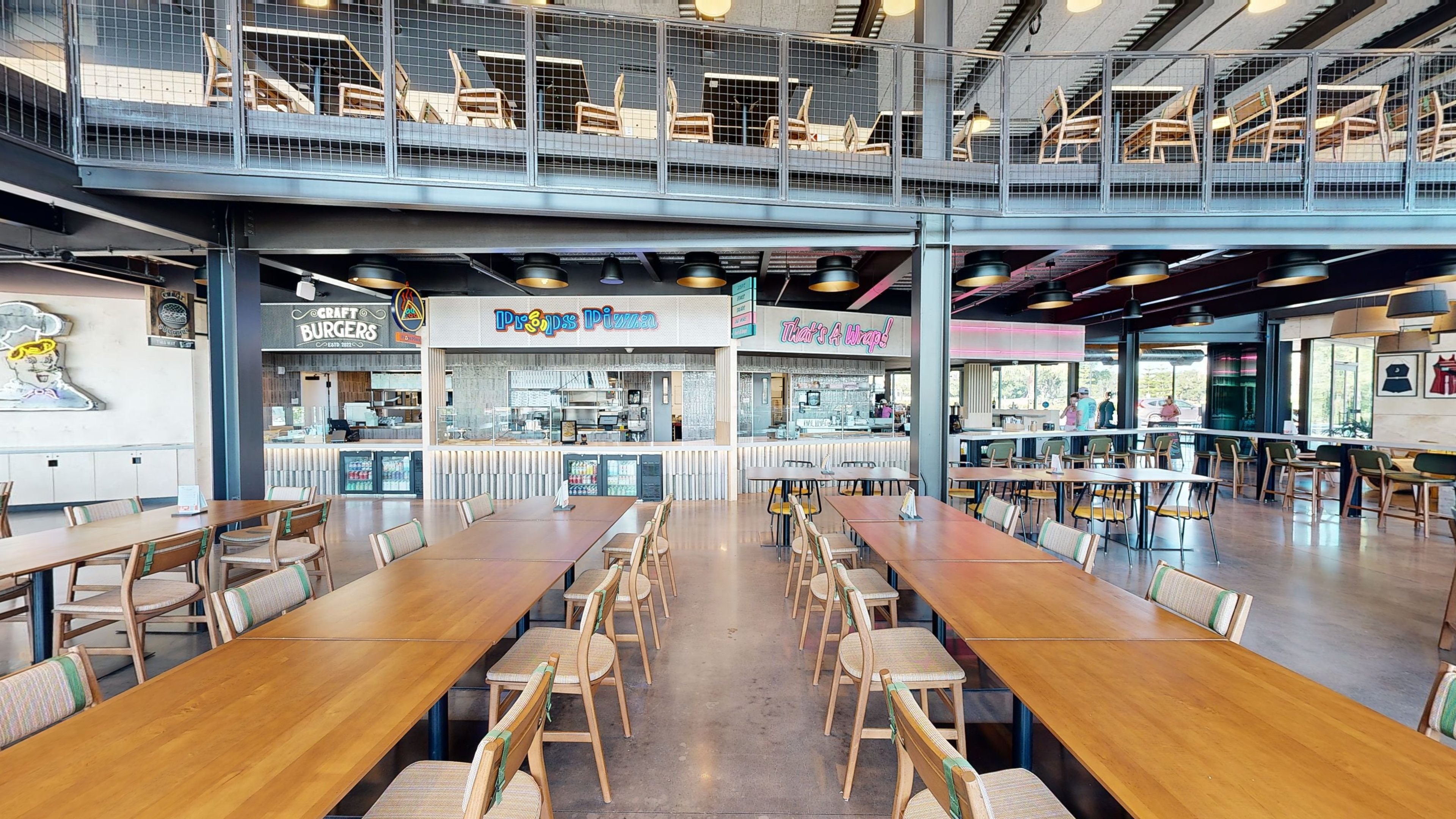 Spacious modern food court with wooden tables, chairs, and various food stalls in the background.