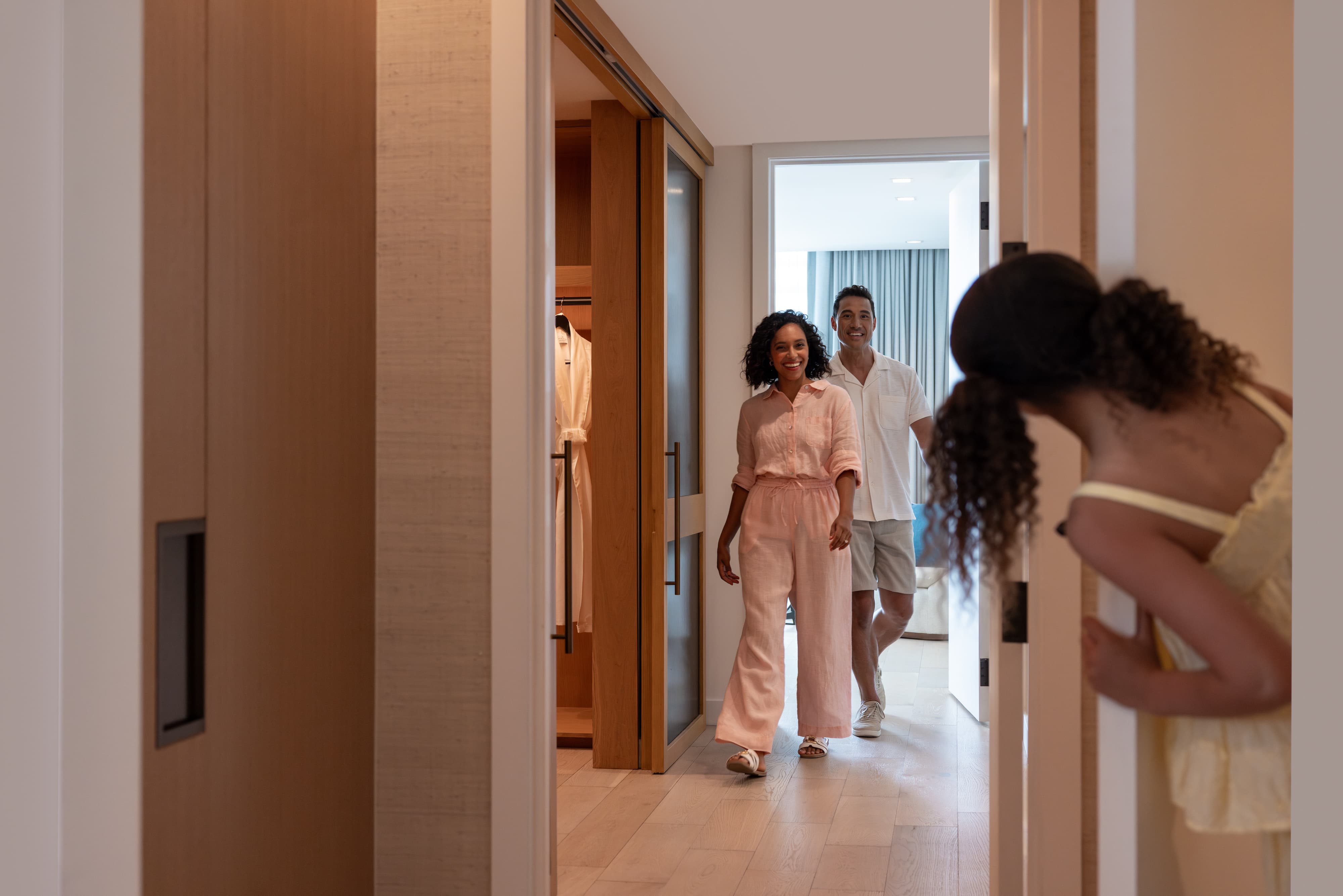 Woman and man entering a room smiling while a child peeks around the doorframe.