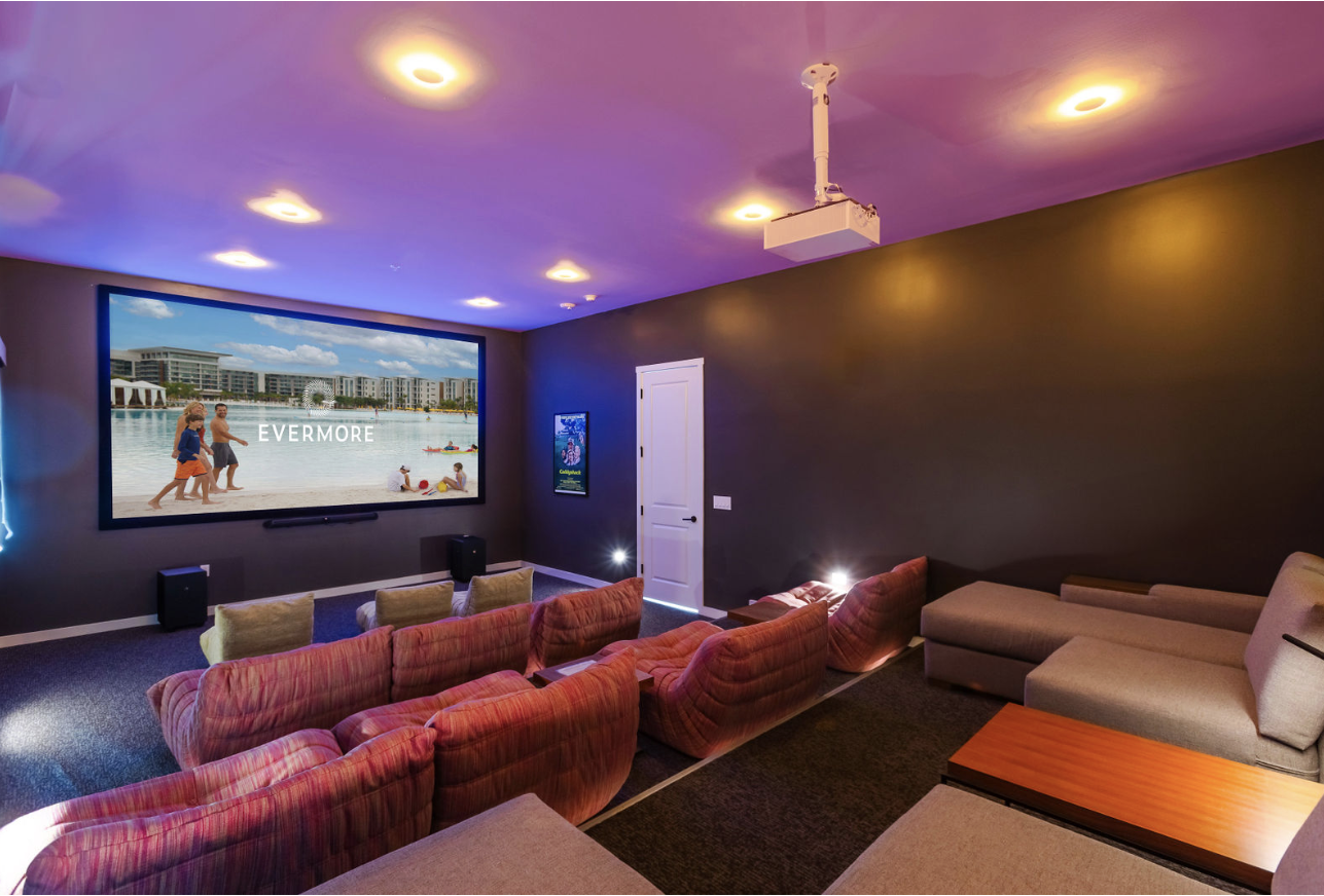 Home theater room with projector, large screen showing beach scene, and rows of plush seating.