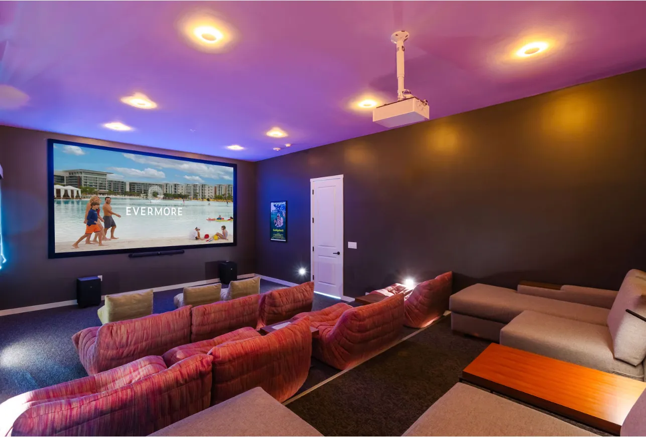 Home theater room with projector, large screen showing beach scene, and rows of plush seating.