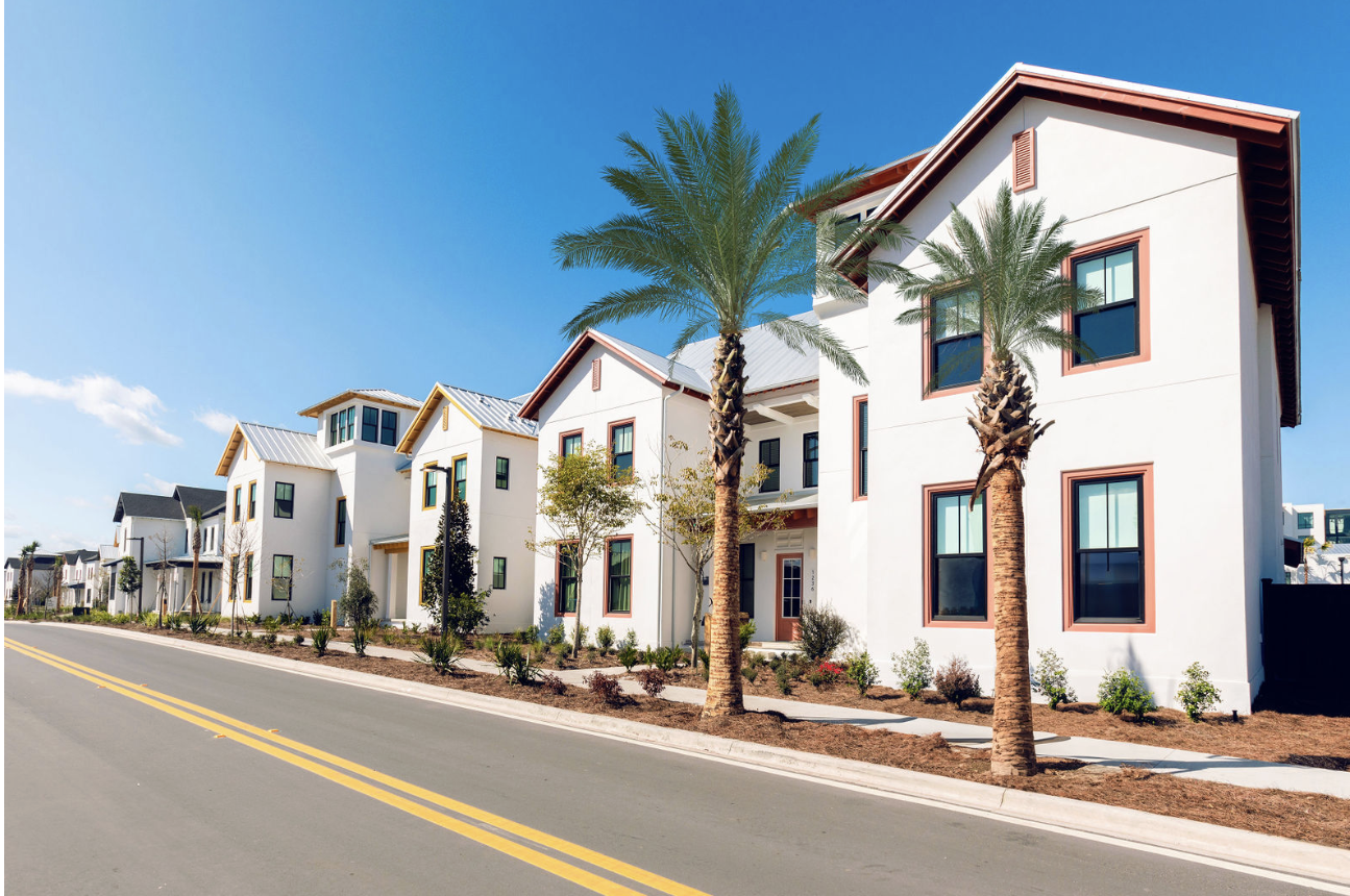 Row of modern white houses with palm trees along a clean street under a clear blue sky.