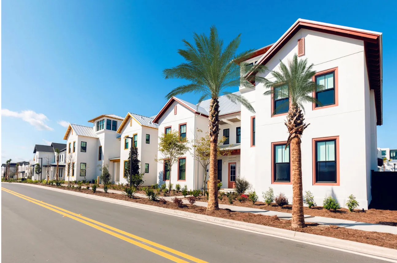 Row of modern white houses with palm trees along a clean street under a clear blue sky.