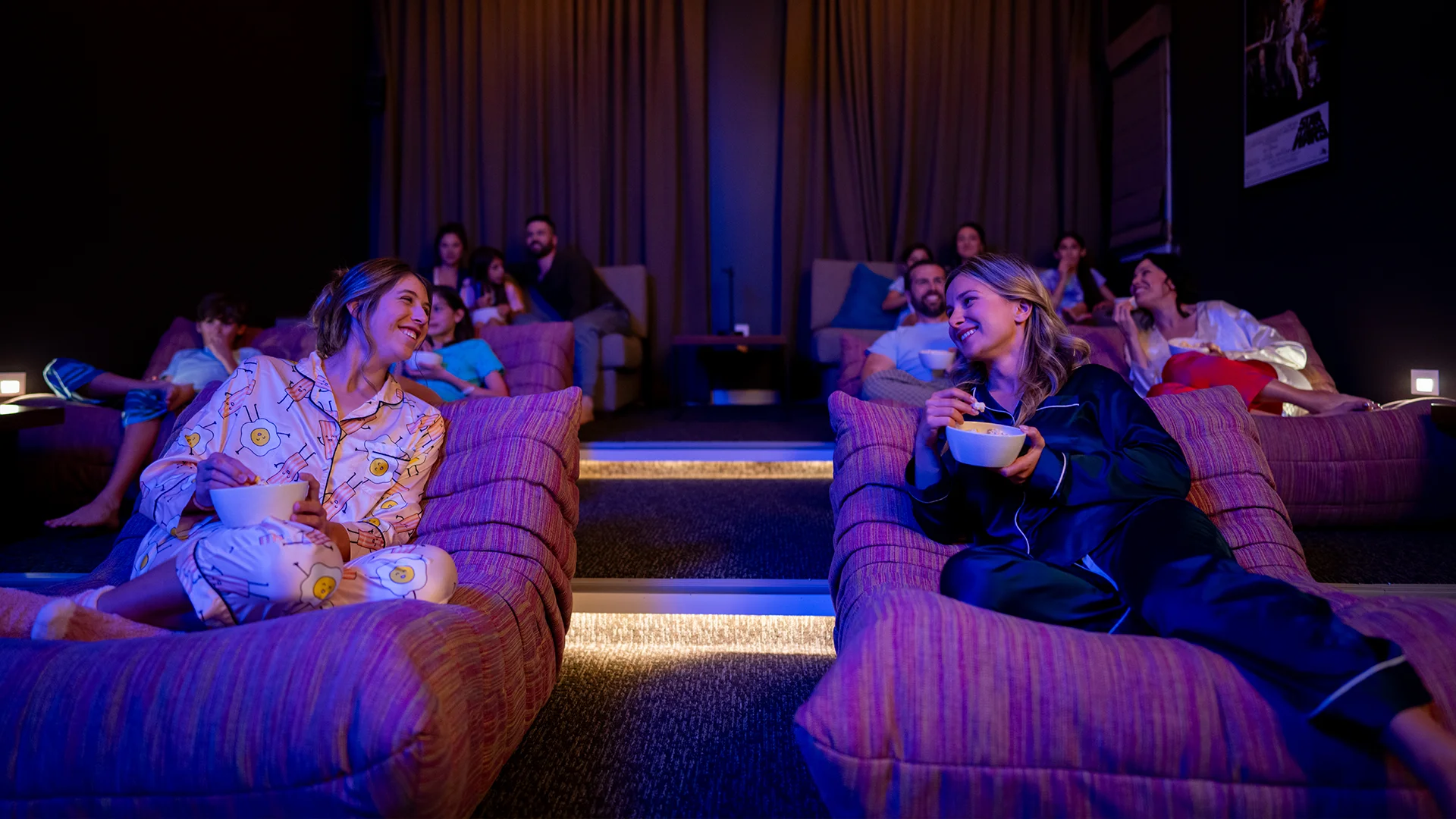 People in pajamas relaxing on lounge chairs in a home theater room eating popcorn.