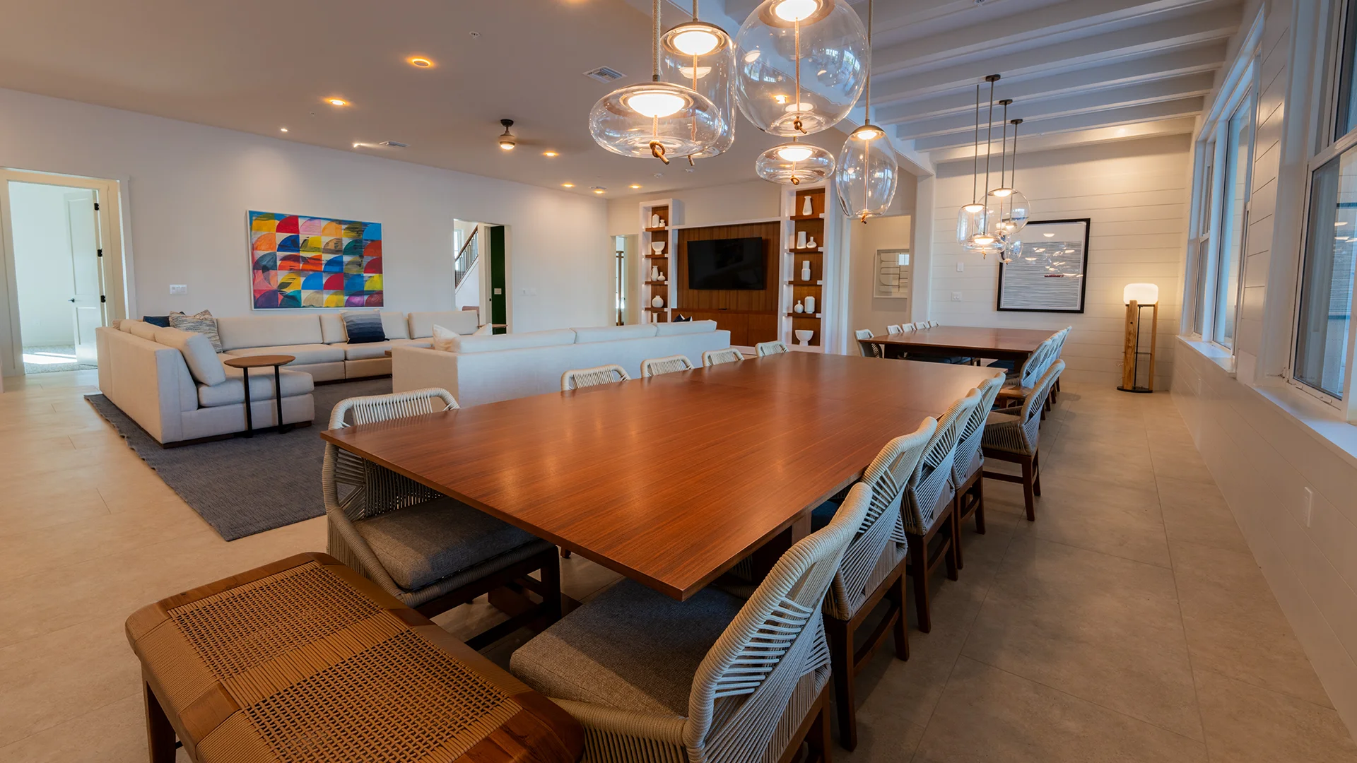 Long wooden dining table with chairs in a spacious modern living and dining room with artwork and pendant lights.