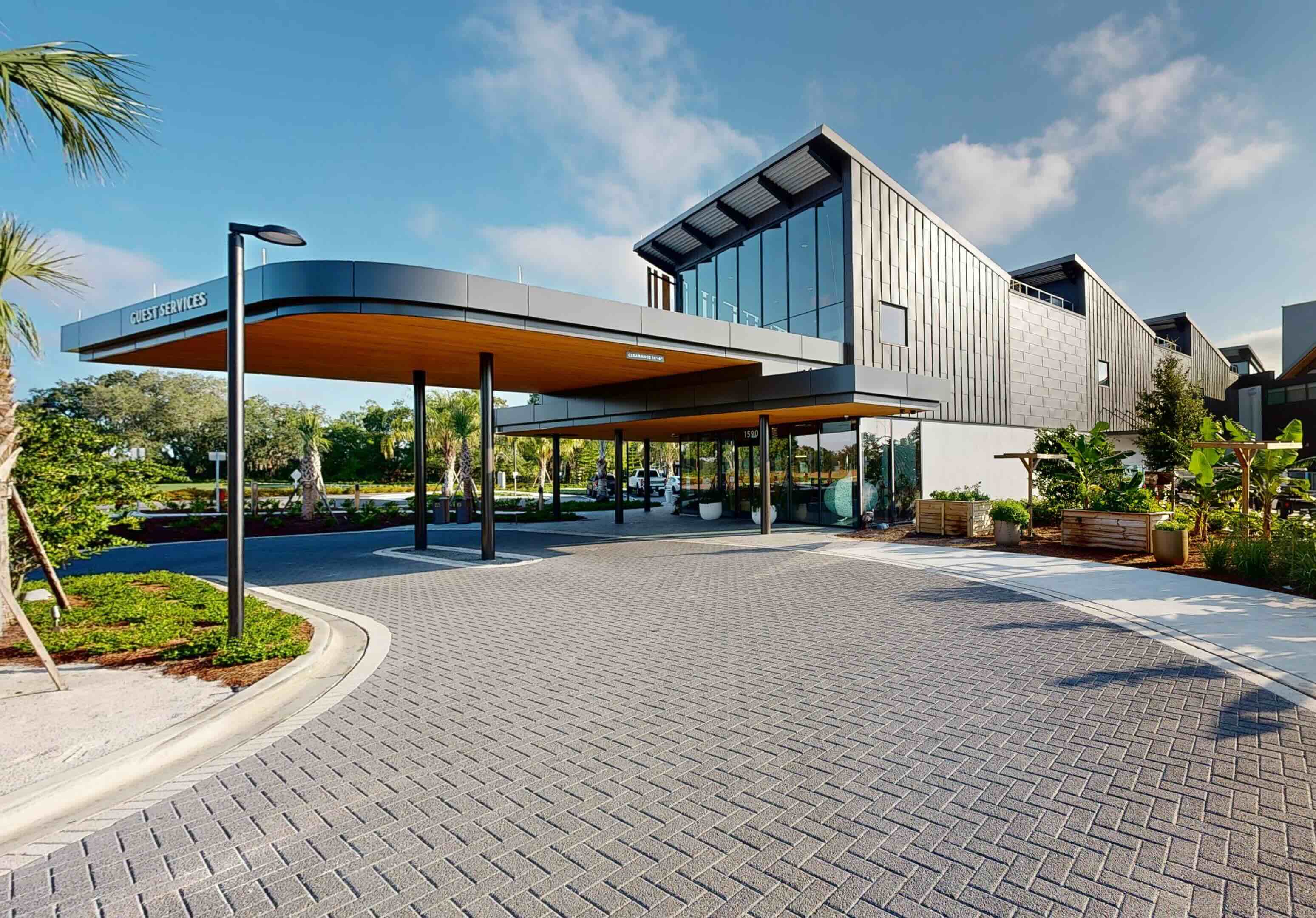 Modern guest services building with glass walls, covered entrance, palm trees, and landscaped surroundings.
