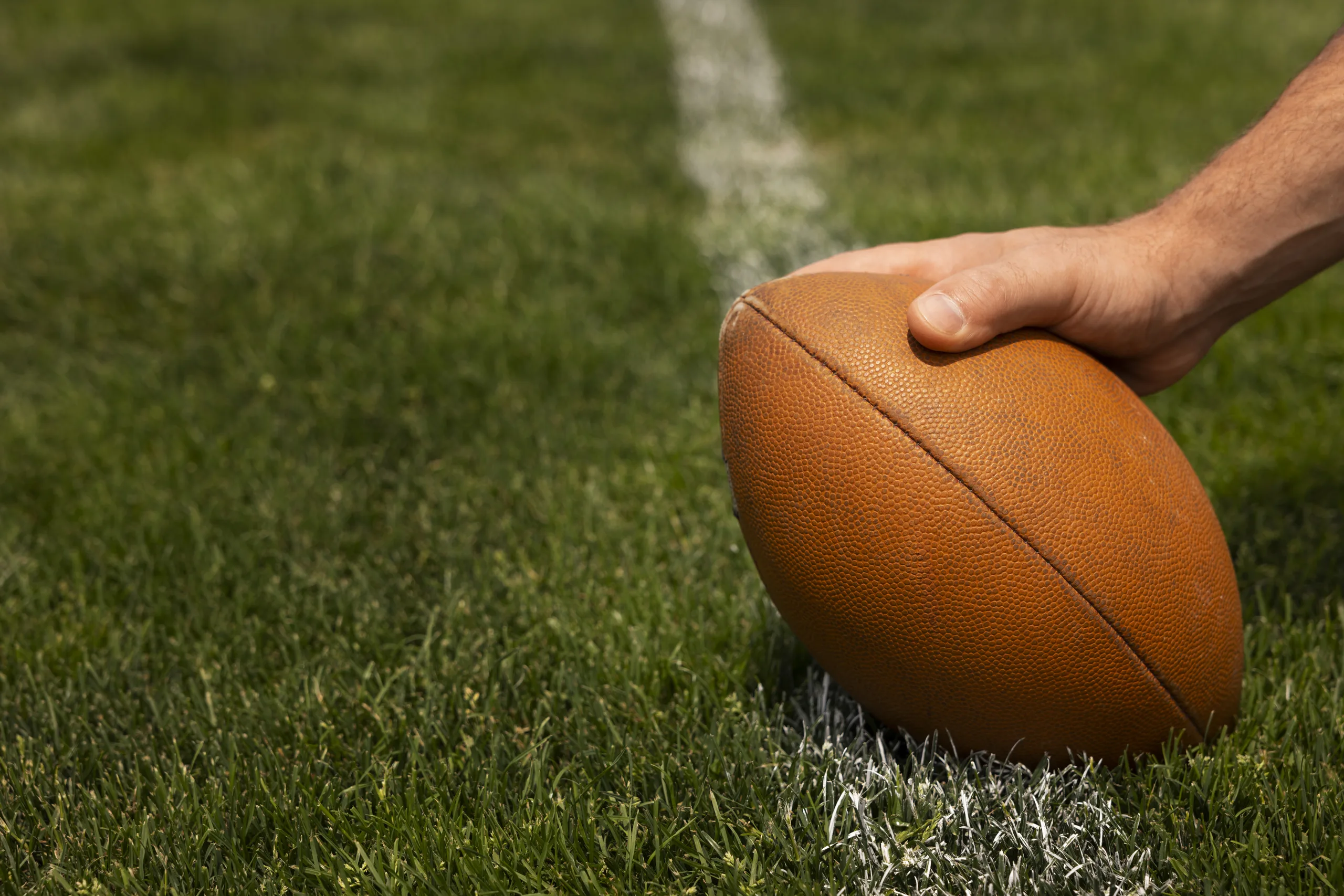 A hand placing an American football on a white line on a green grass field.