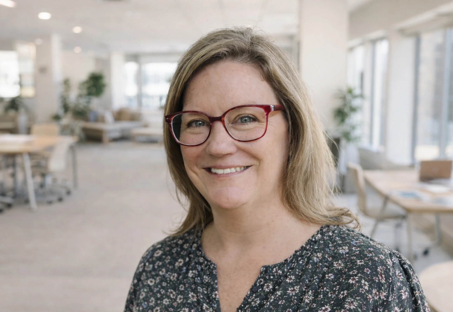 Smiling woman with glasses and floral top in a bright modern office space.