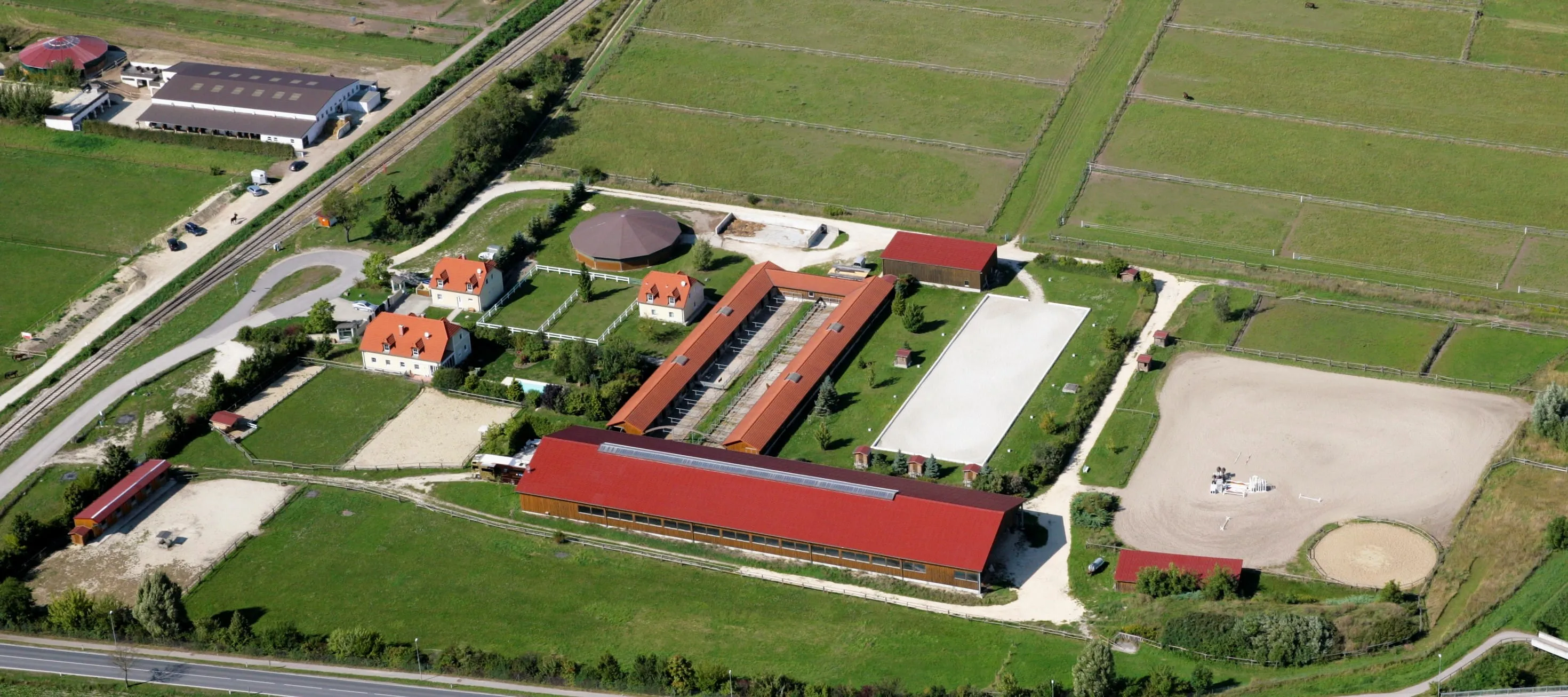 Luftaufnahme einer ländlichen Anlage mit Bauernhöfen, Ställen, Koppeln und Reitplätzen.