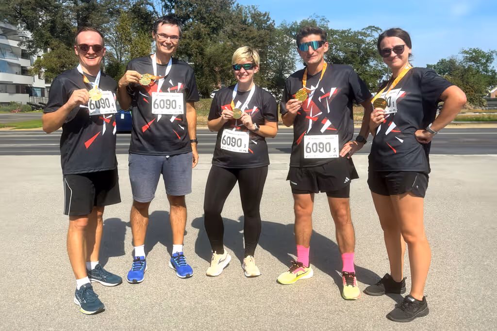 Five people with matching Xfive t-shirts standing together, smiling and presenting their Poland Business Run medals.