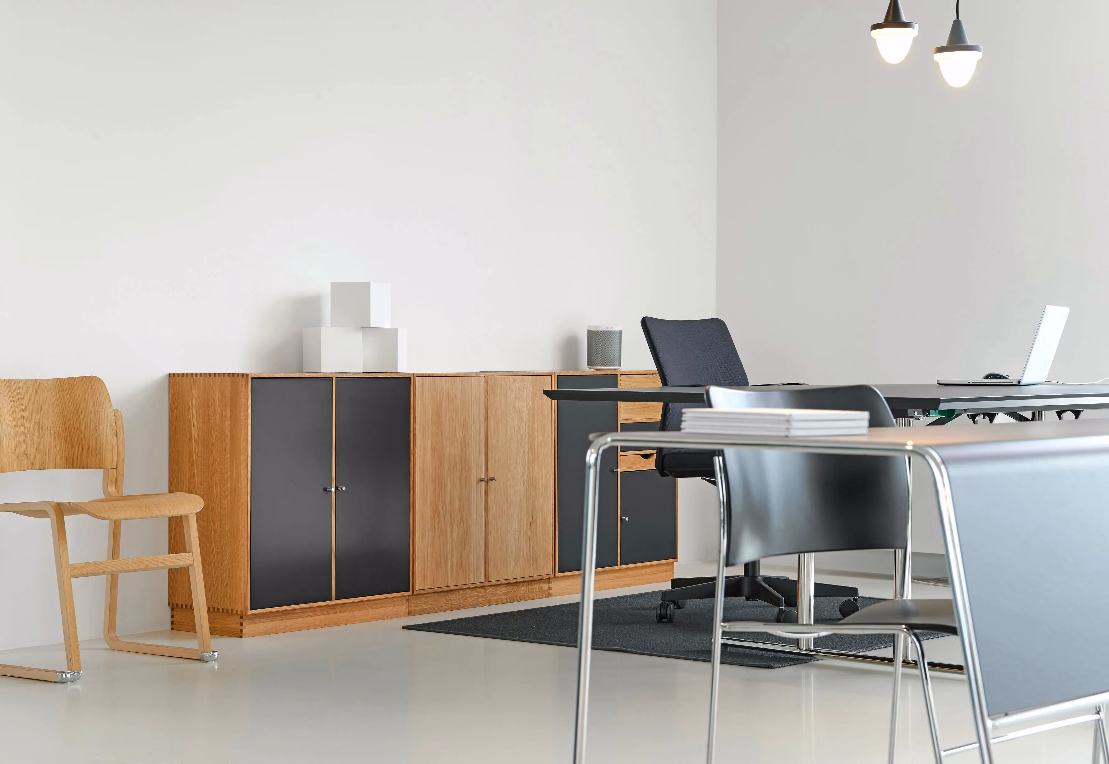 Werkruimte met een houten dressoir met zwarte deuren, bureaustoel en vergadertafel