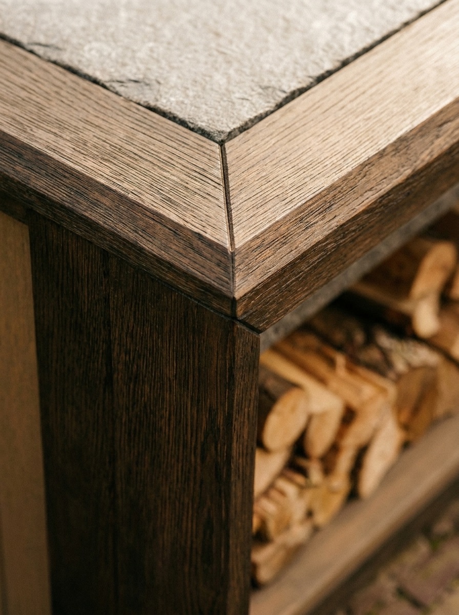 Hoekdetail van het natuurstenen werkblad op het donkere houten onderstel, met haardhout eronder