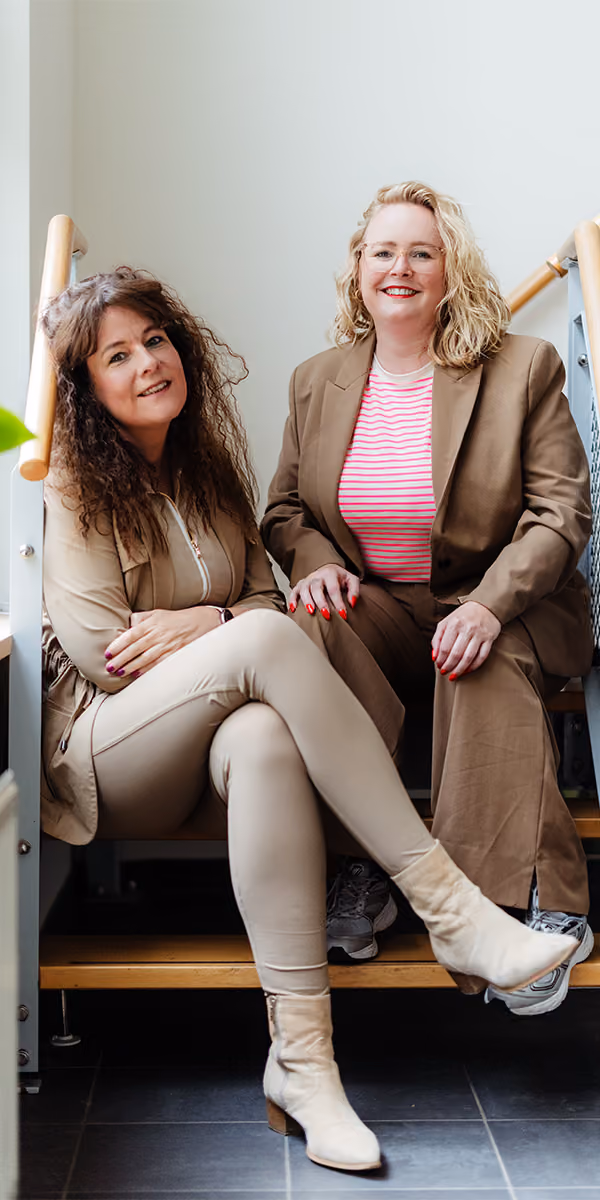 Carolien en Jolien, relatiecounselors bij Voordeliefde, zitten samen lachend op een trap