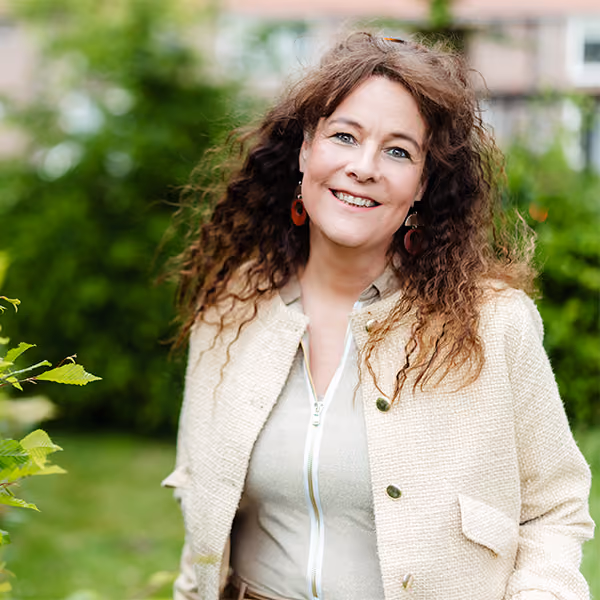 Carolien van Voordeliefde in een beige jas, glimlachend in een groene tuin
