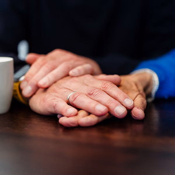 Twee mensen die elkaars handen vasthouden op een houten tafel.
