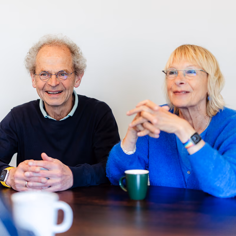 Ouder stel zit glimlachend samen aan tafel met koffie